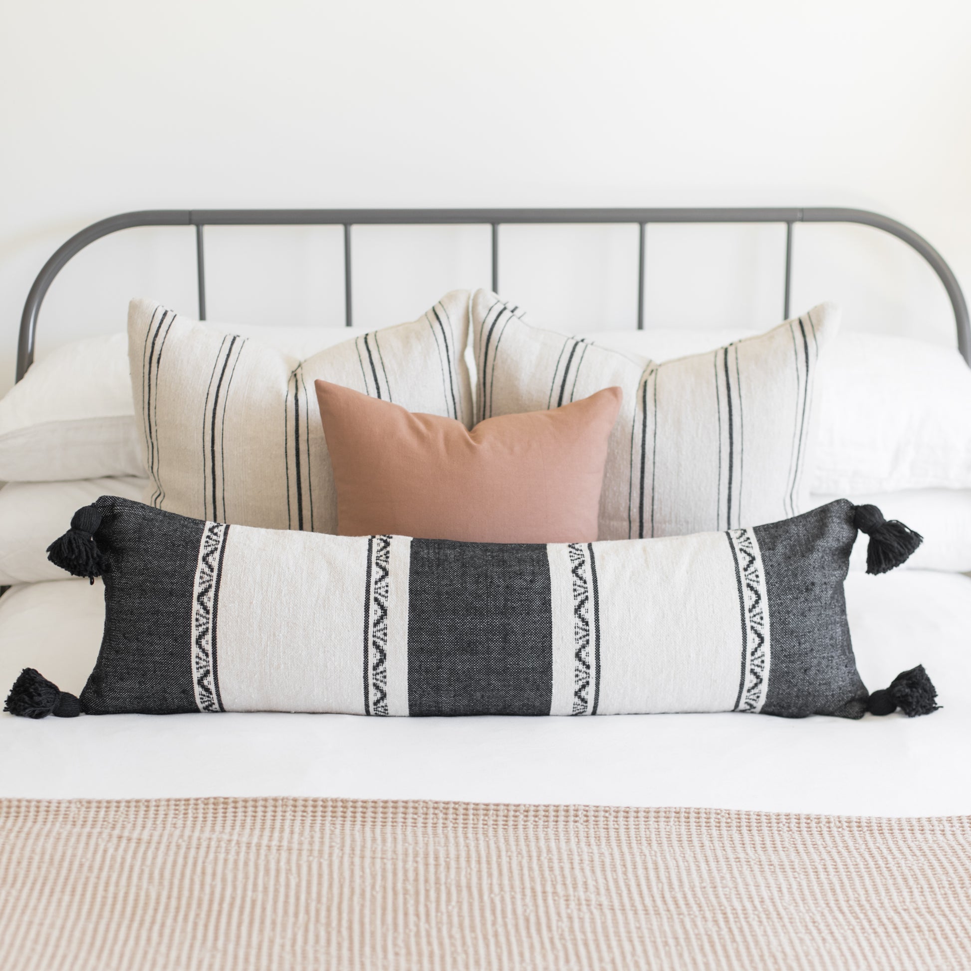 Charcoal and cream striped lumbar pillow with black tassels displayed on a bed with coordinating pillows.