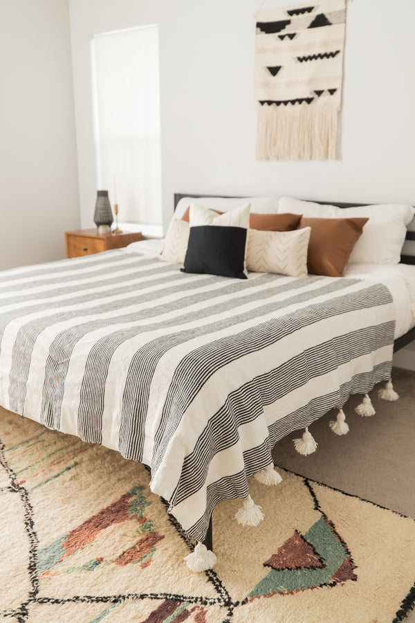 Large striped bedspread with tassel fringe in cream and charcoal gray on a king/queen bed.