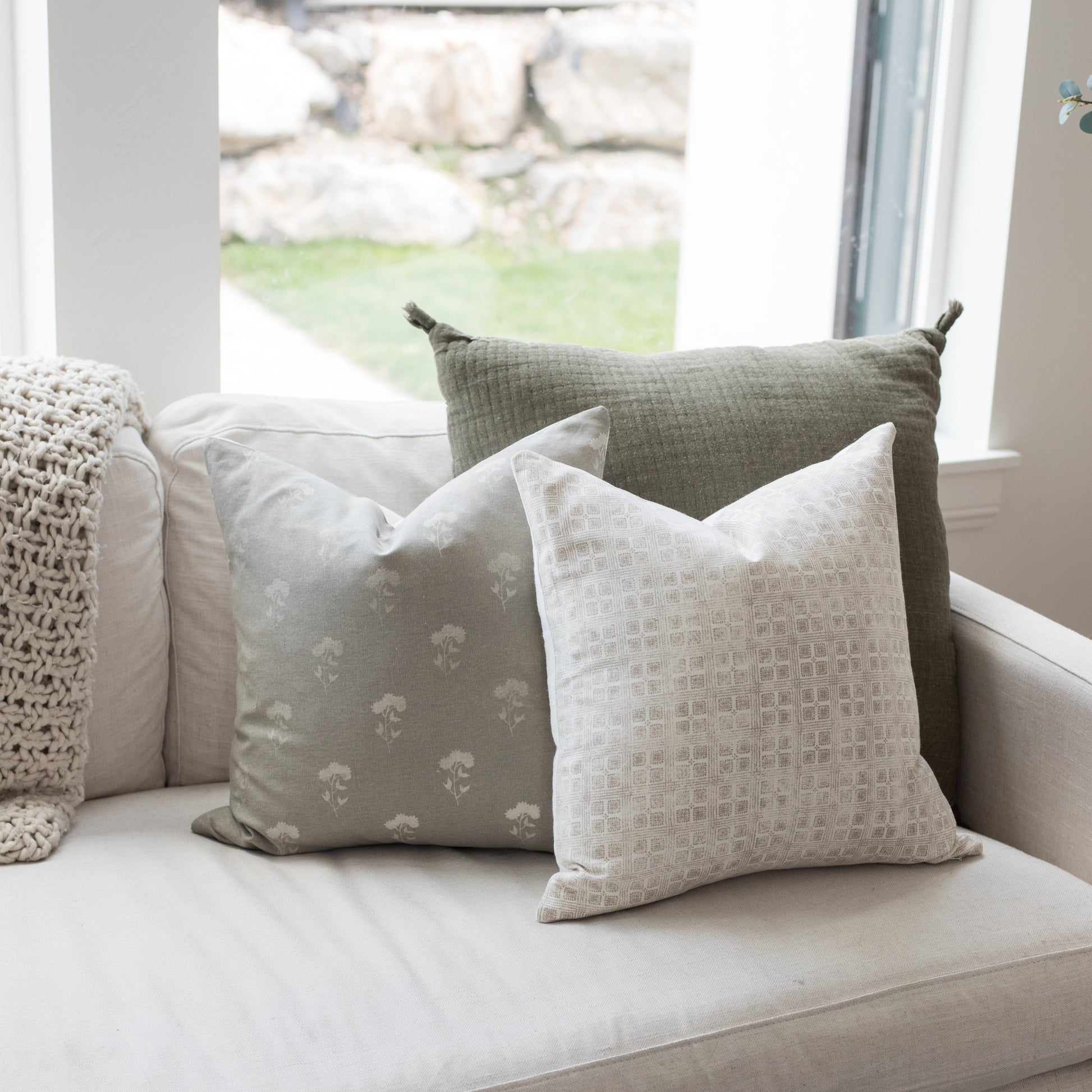 Gray floral pillow with white floral pattern displayed on cream sofa with other textured pillows.