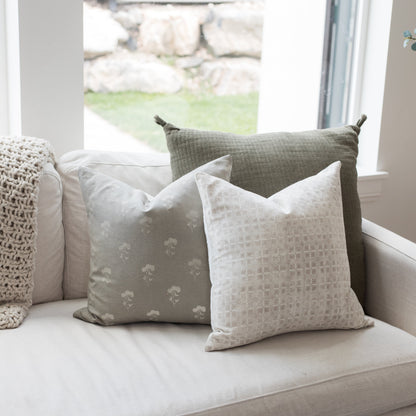 Gray floral pillow with white floral pattern displayed on cream sofa with other textured pillows.