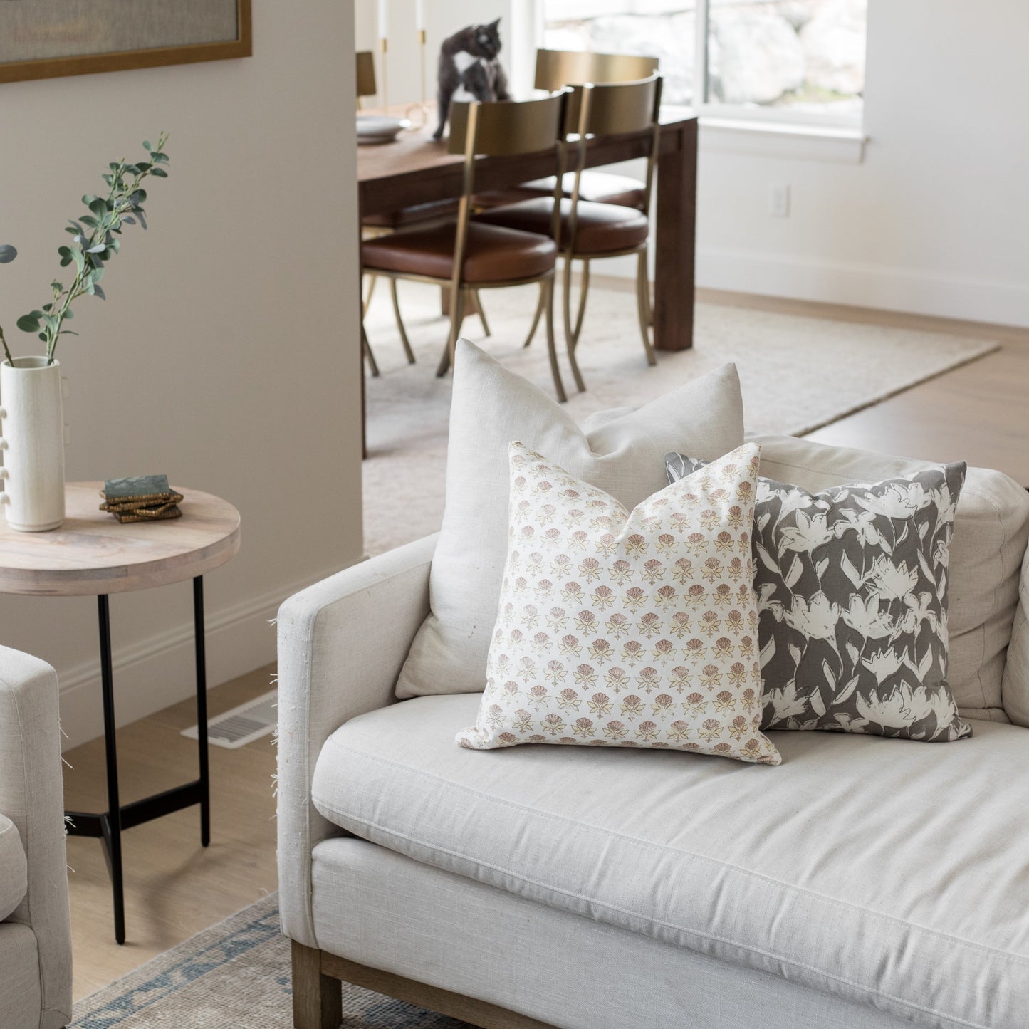 Four 18-inch throw pillows with cream, tan, and charcoal floral and geometric patterns arranged on a cream sofa.
