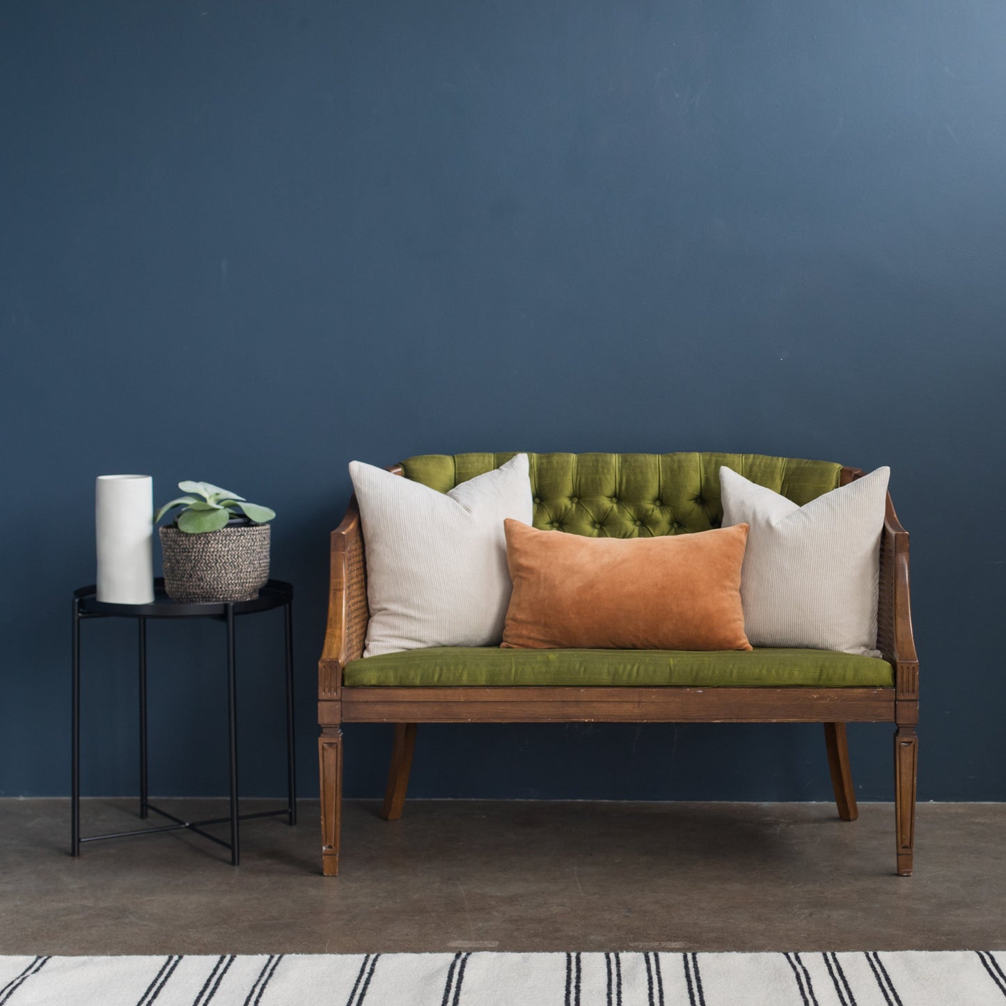 Rust velvet lumbar pillow displayed on wooden sofa with white and green cushions.