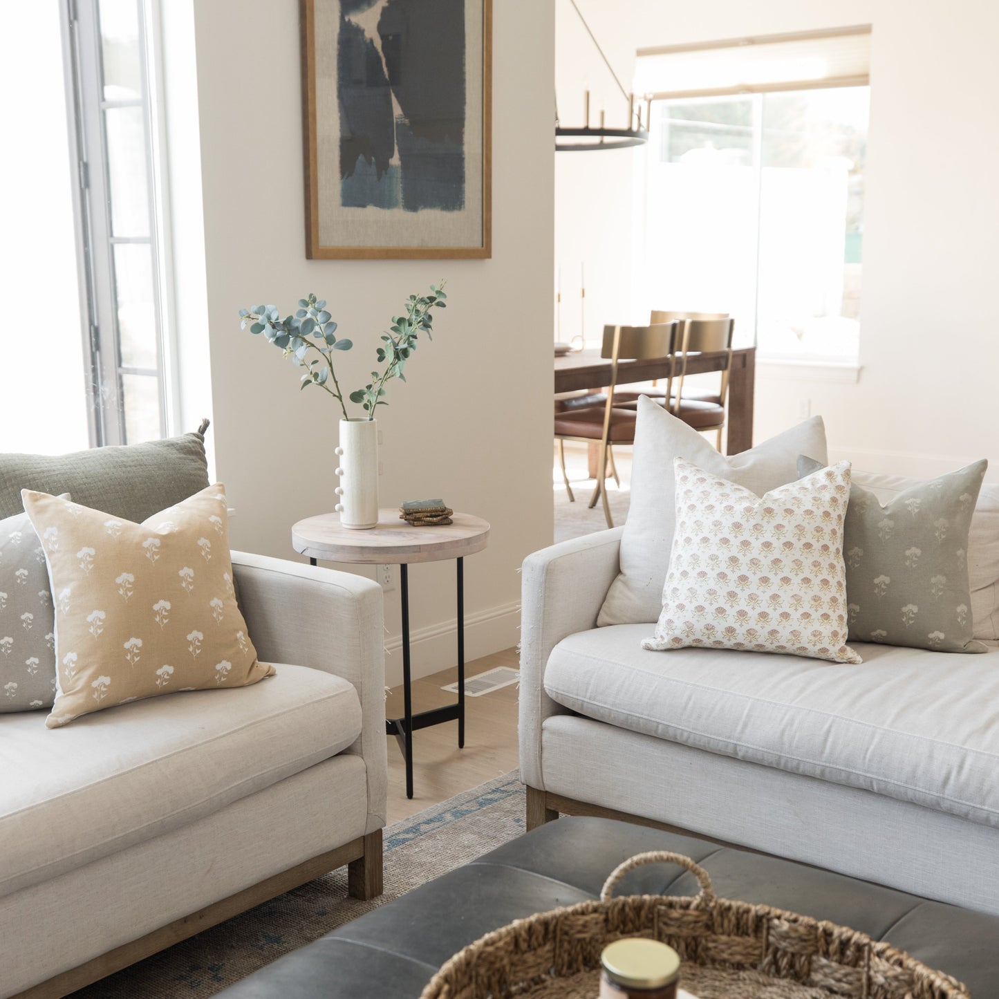 Four 18-inch square throw pillows with neutral and patterned designs displayed on cream-colored sofas in a living room.