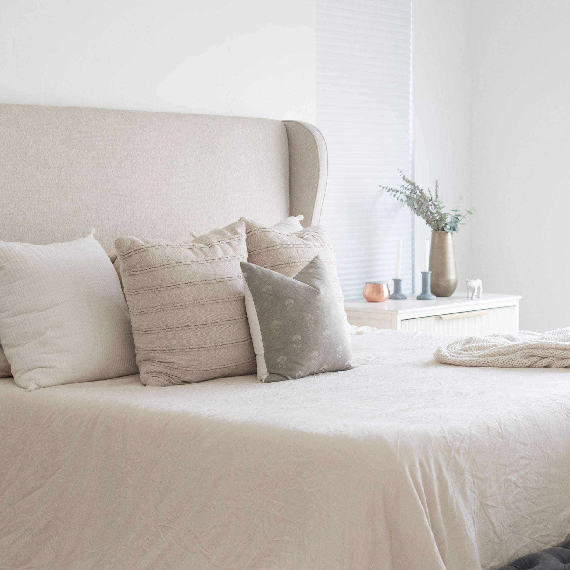 Gray throw pillow with subtle floral pattern displayed on bed with neutral bedding.