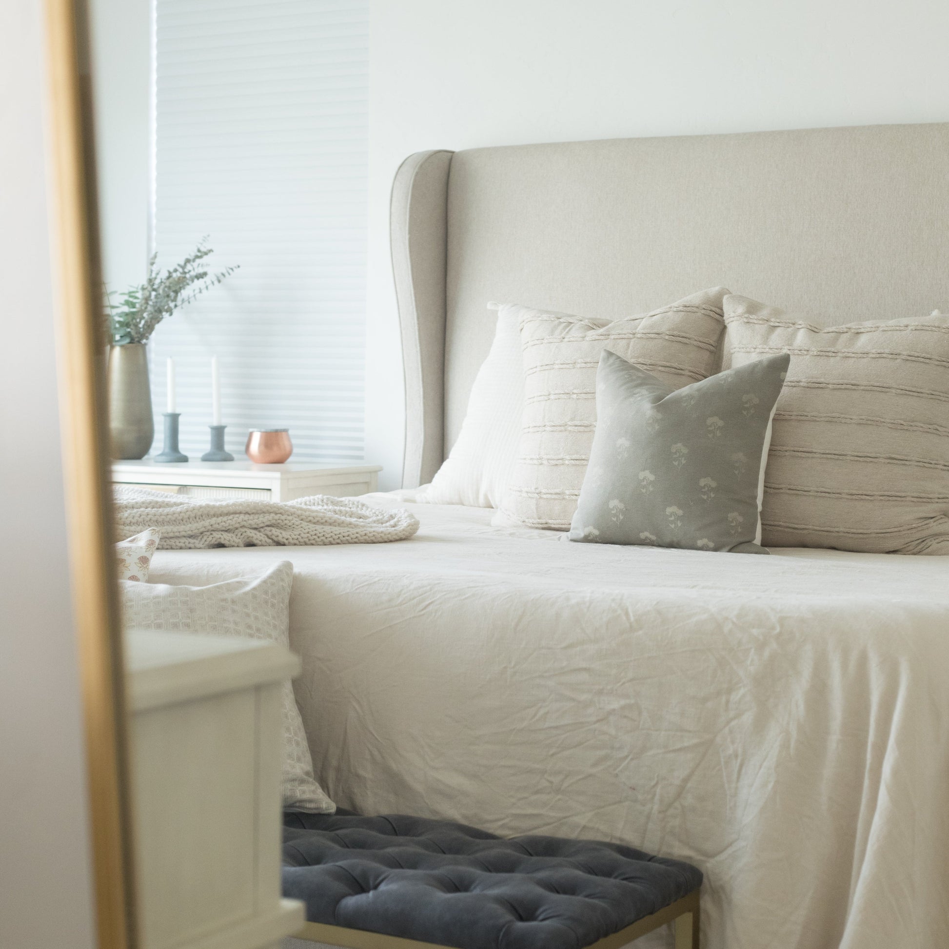 Gray floral throw pillow on a bed with cream bedding and upholstered headboard.