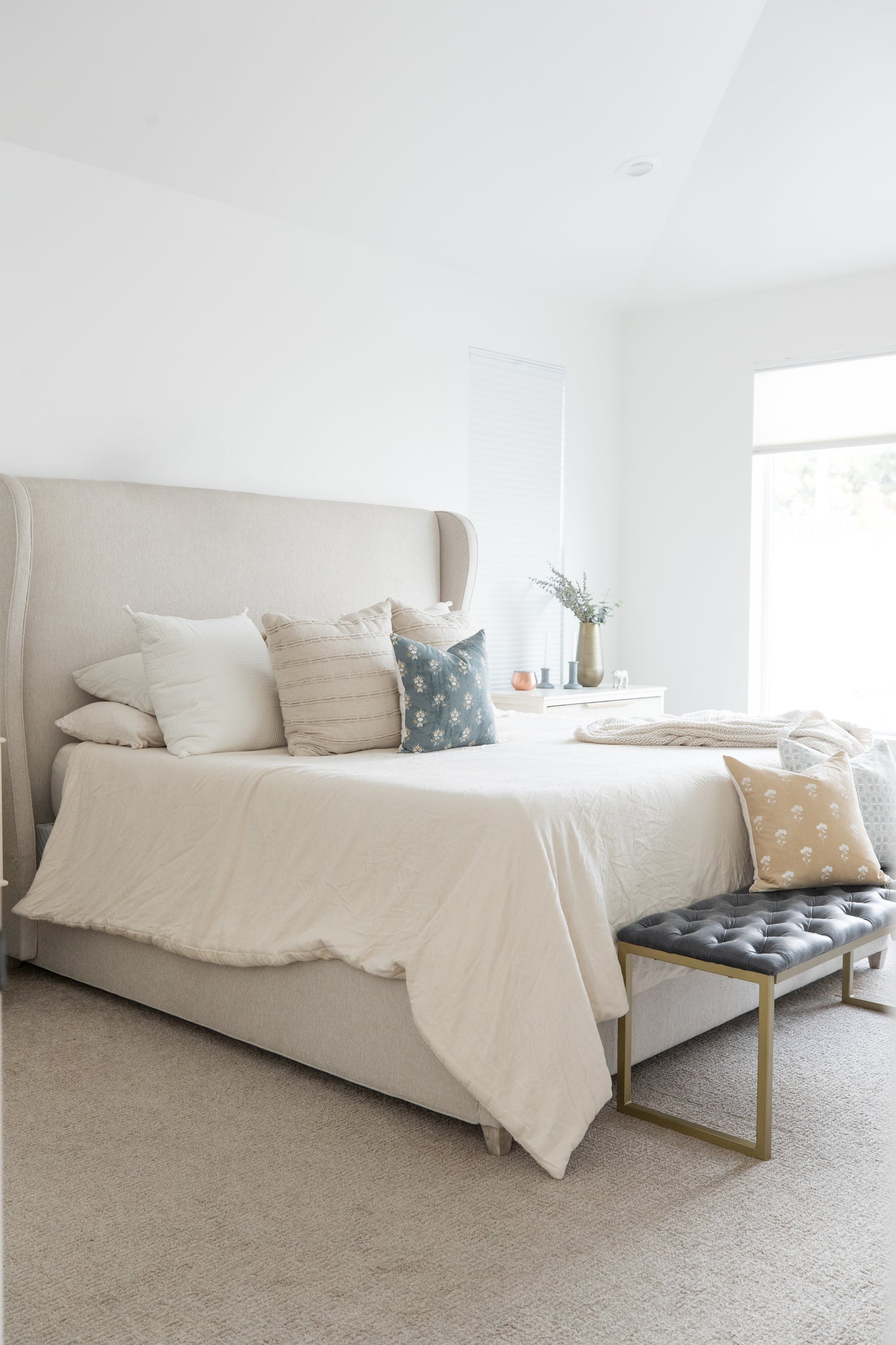 Four decorative pillows in cream, striped, blue floral, and tan patterns arranged on a bed with white bedding.