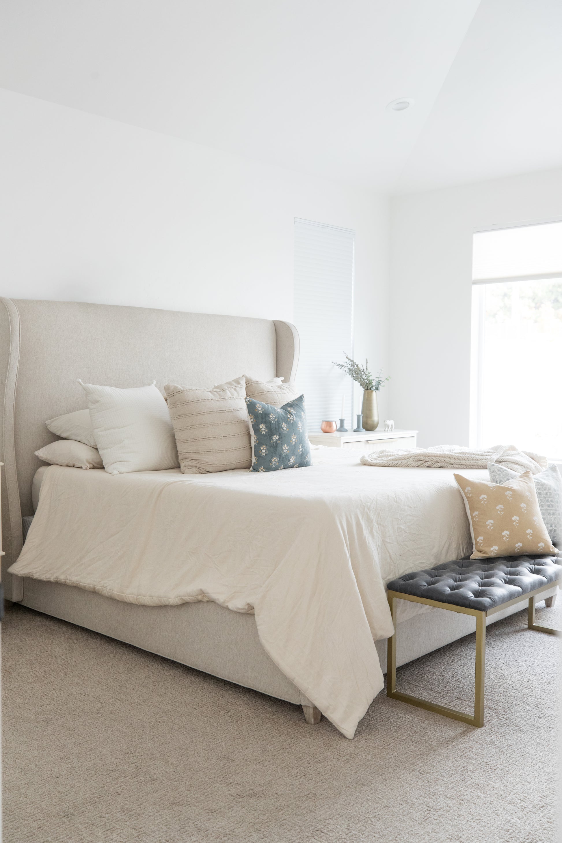 Four decorative pillows in cream, striped, blue floral, and tan patterns arranged on a bed with white bedding.