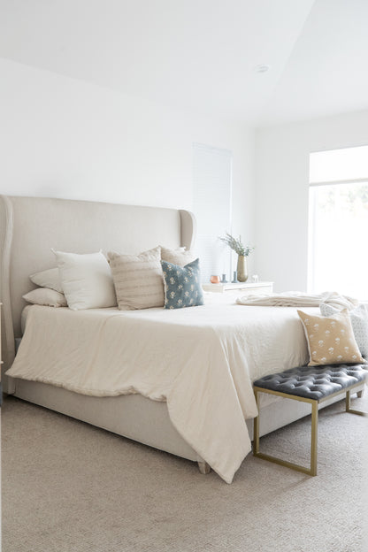 Four decorative pillows in cream, striped, blue floral, and tan patterns arranged on a bed with white bedding.