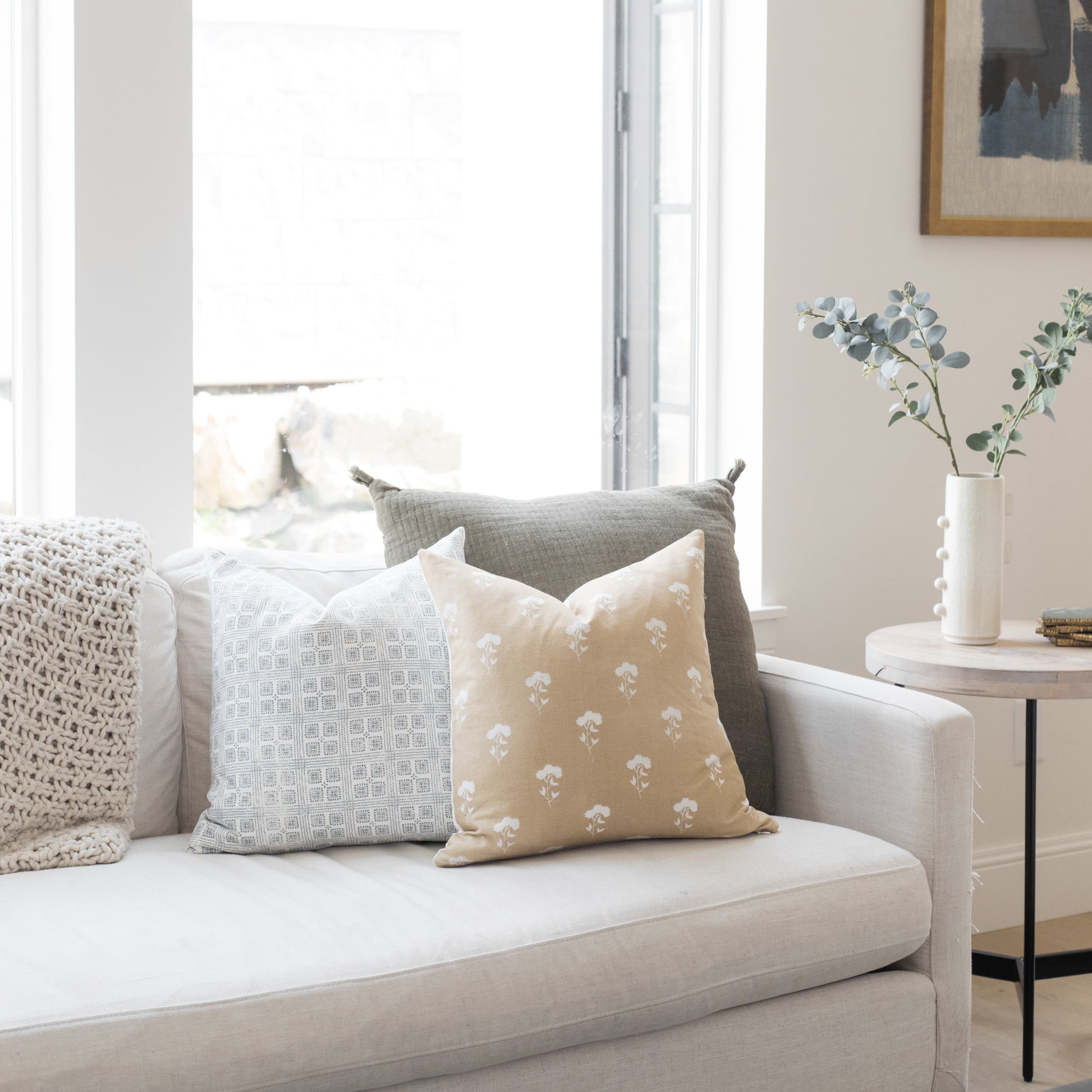 Four decorative pillows in neutral tones with geometric and floral patterns arranged on a light gray sofa.