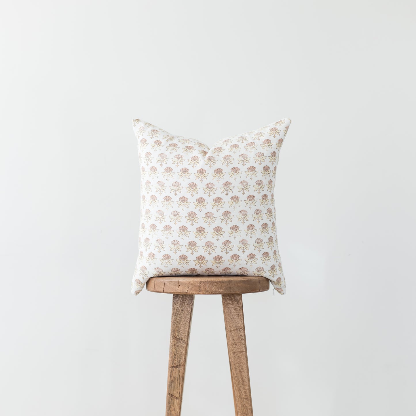 Cream pillow with tan floral pattern displayed on wooden stool against gray background.