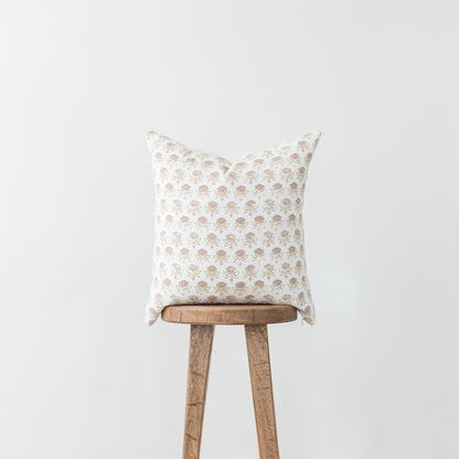 Cream pillow with tan floral pattern displayed on wooden stool against gray background.