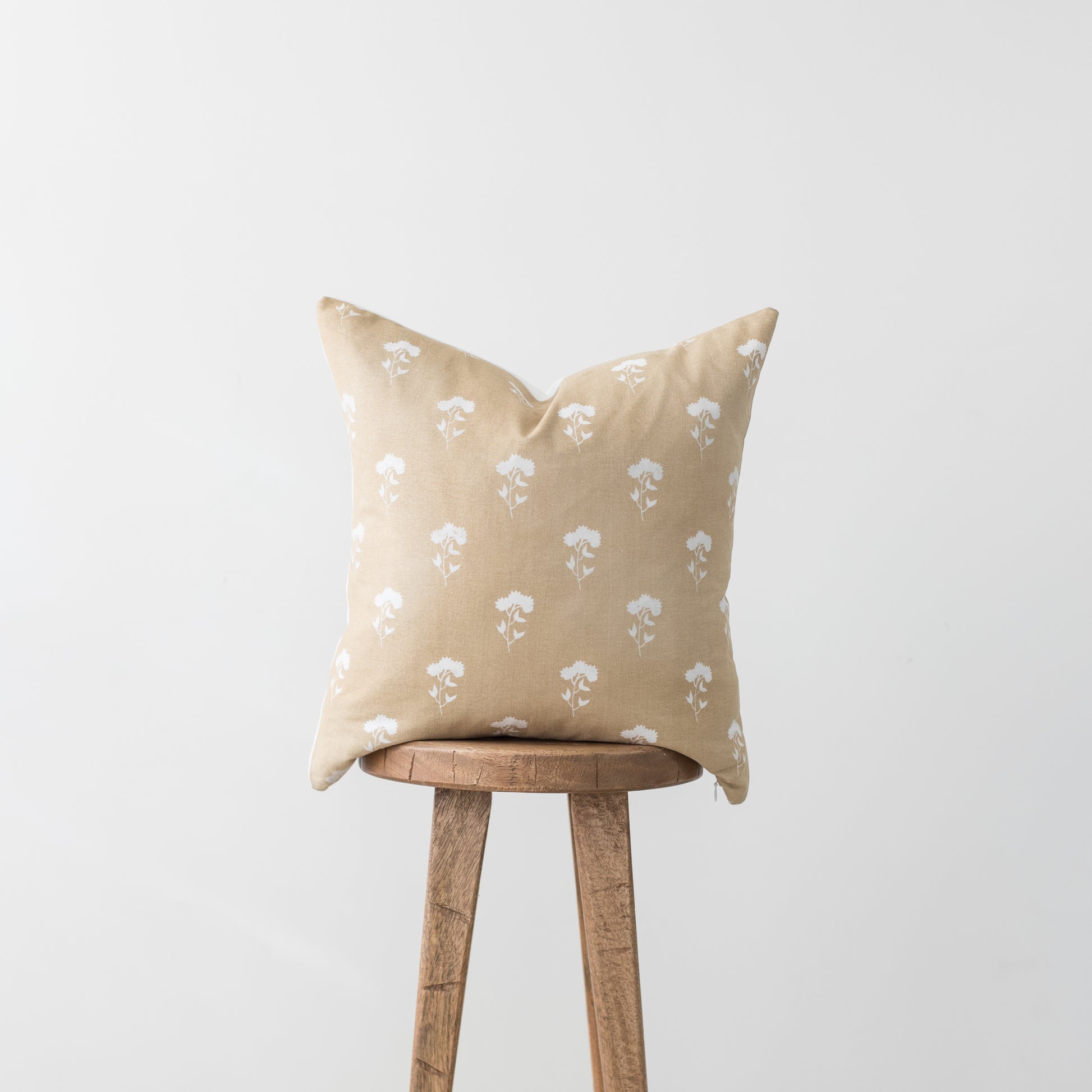 Beige linen pillow with white floral print pattern, displayed on a wooden stool.