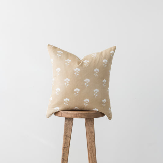 Beige linen pillow with white floral print pattern, displayed on a wooden stool.