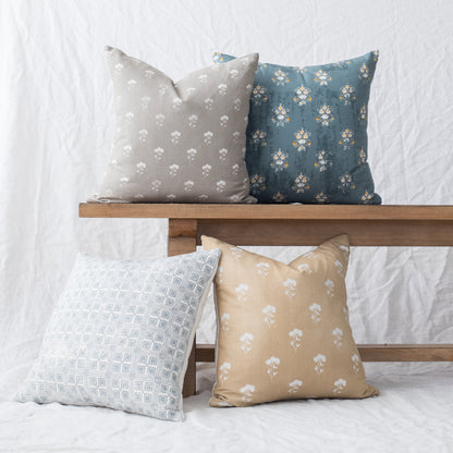 Four decorative pillows with floral and geometric patterns in cream, blue, and tan displayed on wooden shelf.