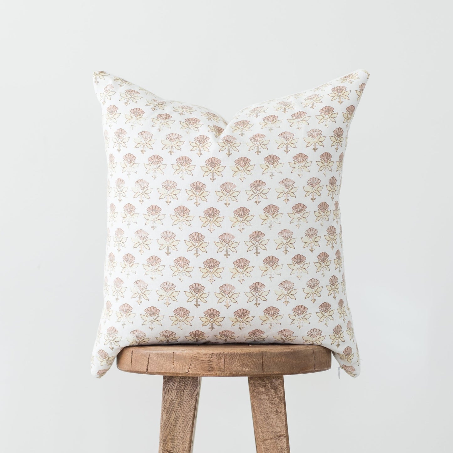 White pillow with tan and pink floral botanical pattern displayed on wooden stool.