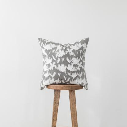 Gray and white floral patterned pillow with white flowers and green leaves on wooden stool.
