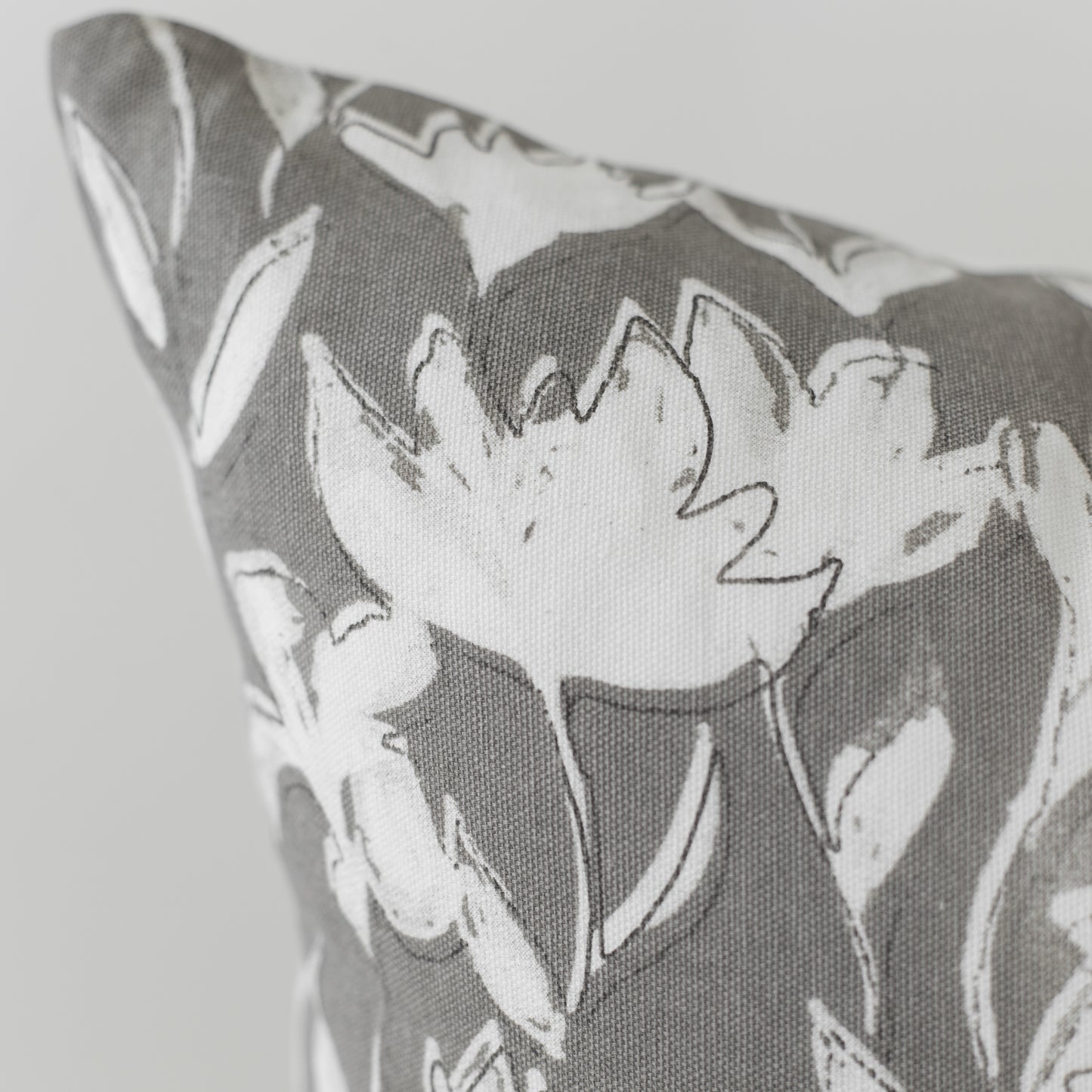Gray and white pillow with outlined floral pattern on textured fabric.