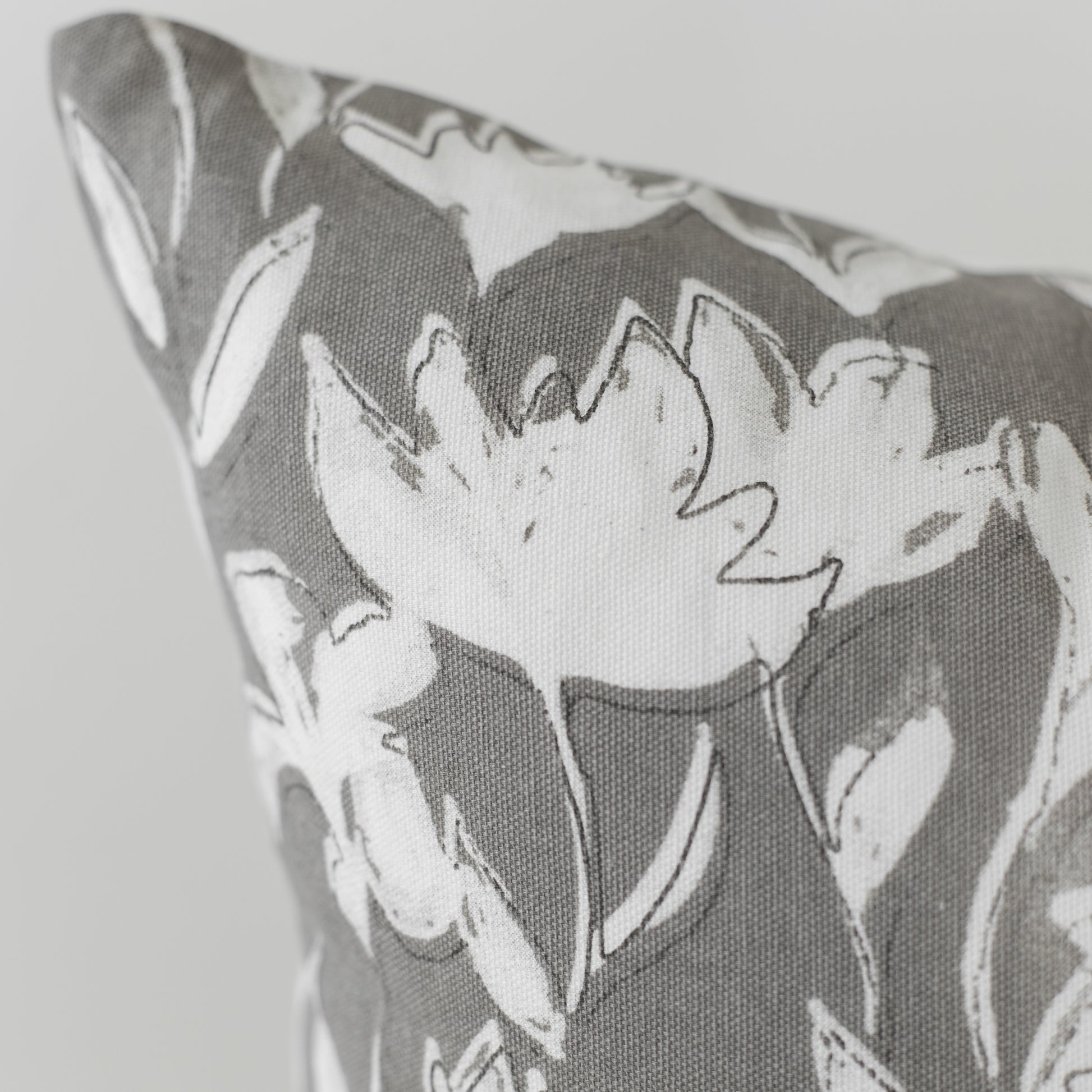 Gray and white pillow with outlined floral pattern on textured fabric.