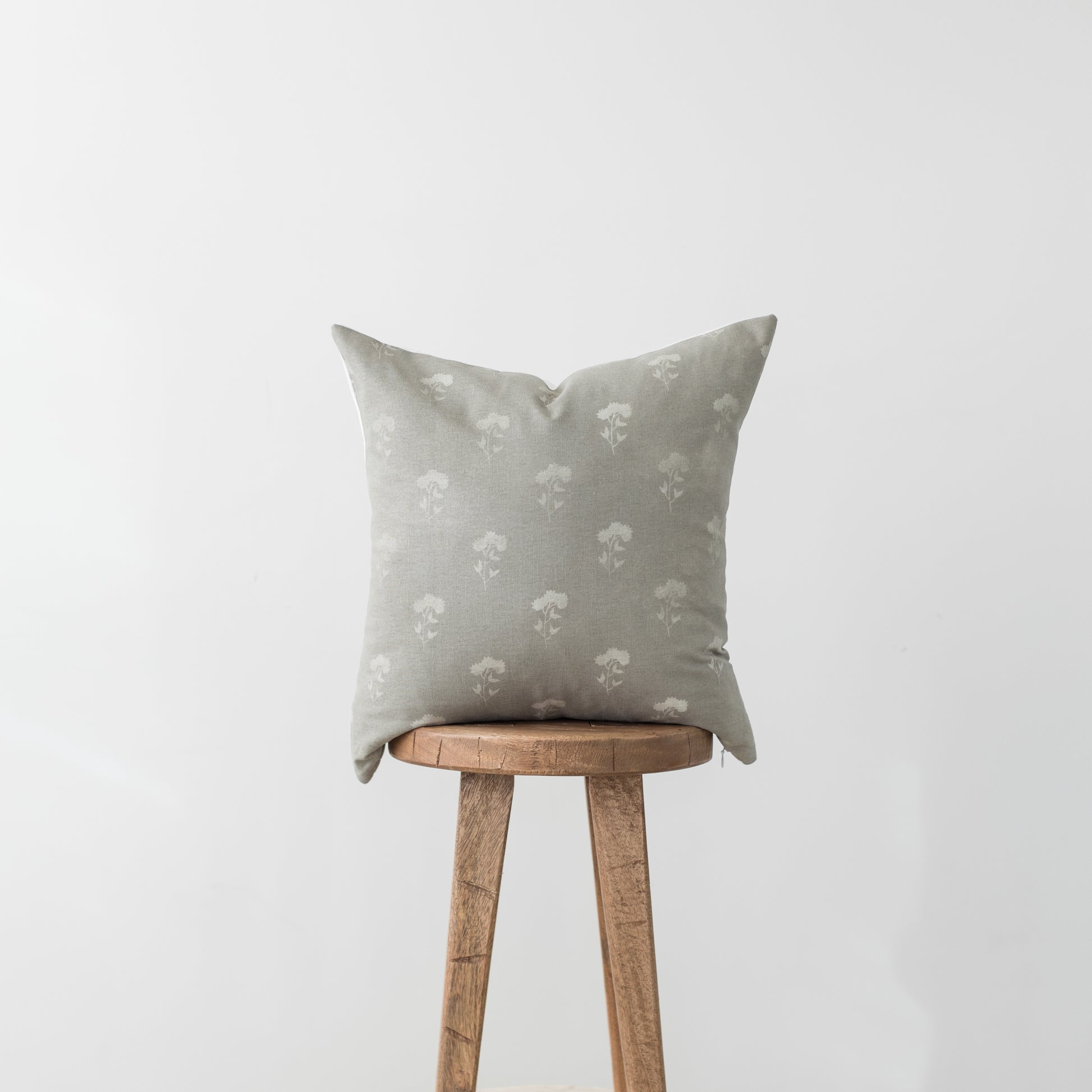 Beige linen pillow with white floral pattern displayed on wooden stool.