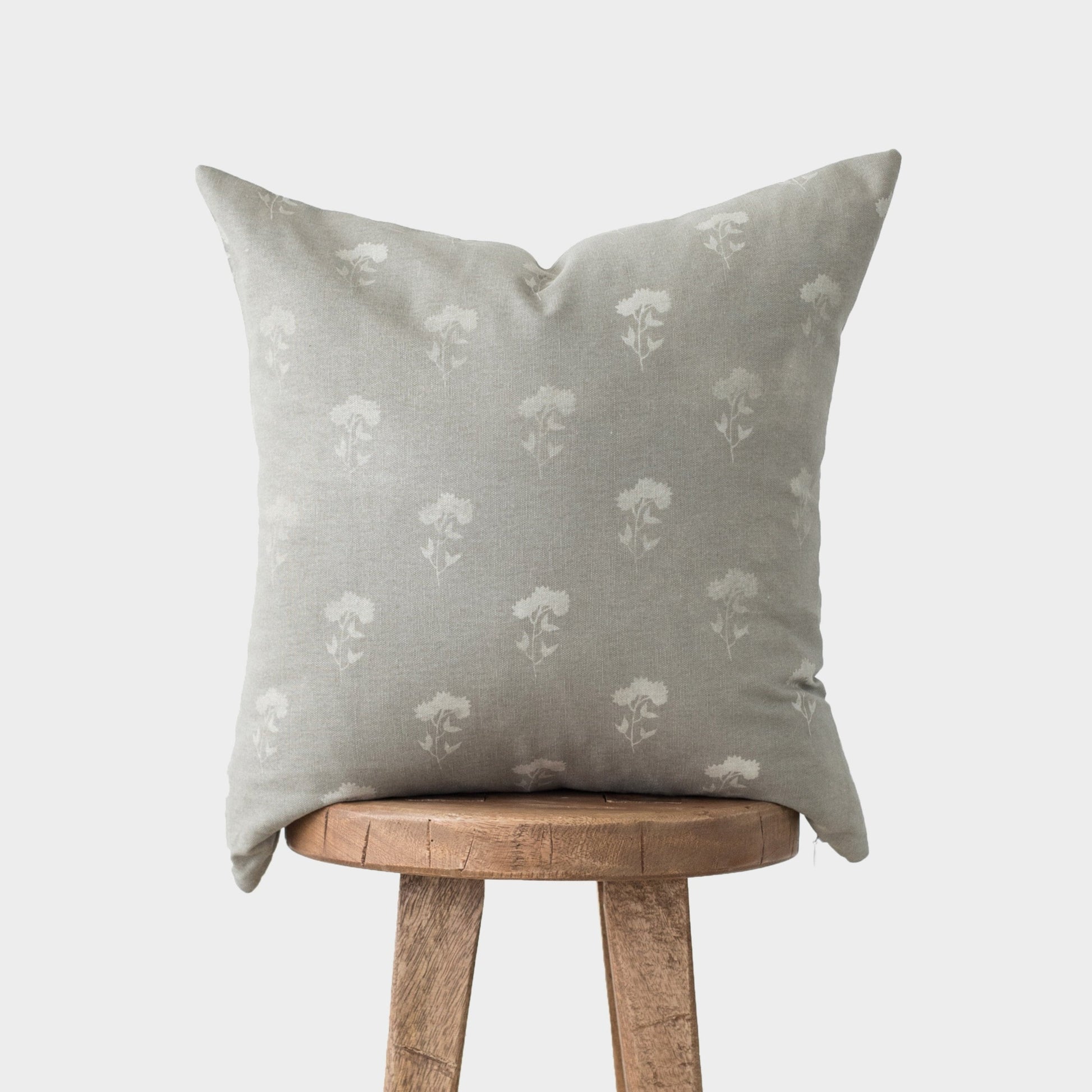 Gray linen pillow with white floral print pattern, displayed on wooden stool.
