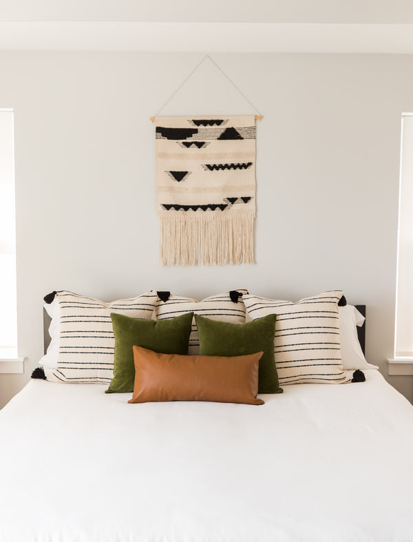 Milo lumbar pillow in cream with black geometric patterns, displayed on bed with green and cognac pillows.