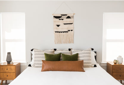Rectangular lumbar pillow in cognac brown leather displayed on bed with striped and green pillows.