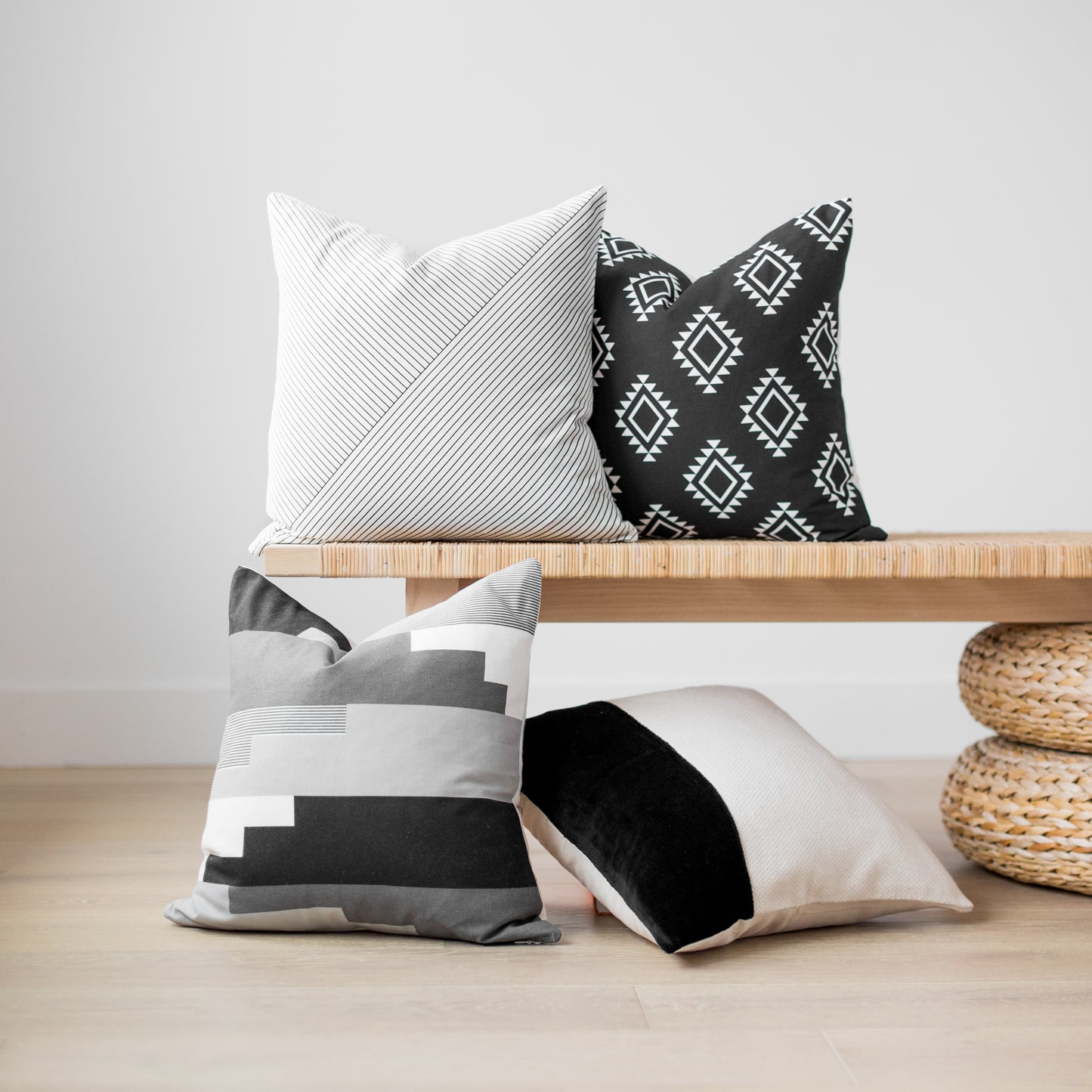 Four 18" decorative pillows in white striped, black geometric, gray colorblock, and black velvet patterns displayed on wooden