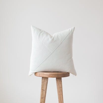 White striped throw pillow with diagonal pattern displayed on wooden stool.