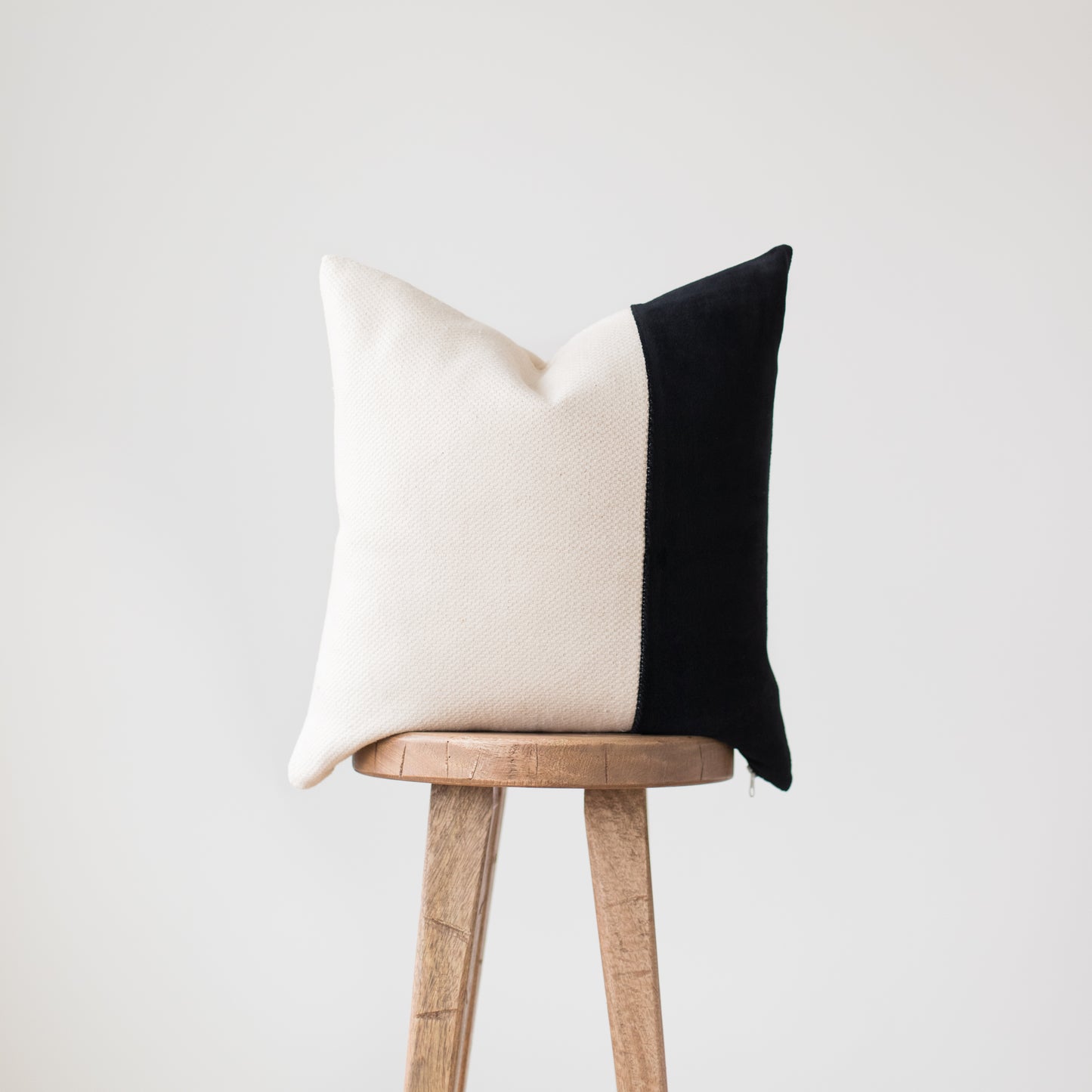 Square throw pillow with cream and black color-block design on wooden stool.