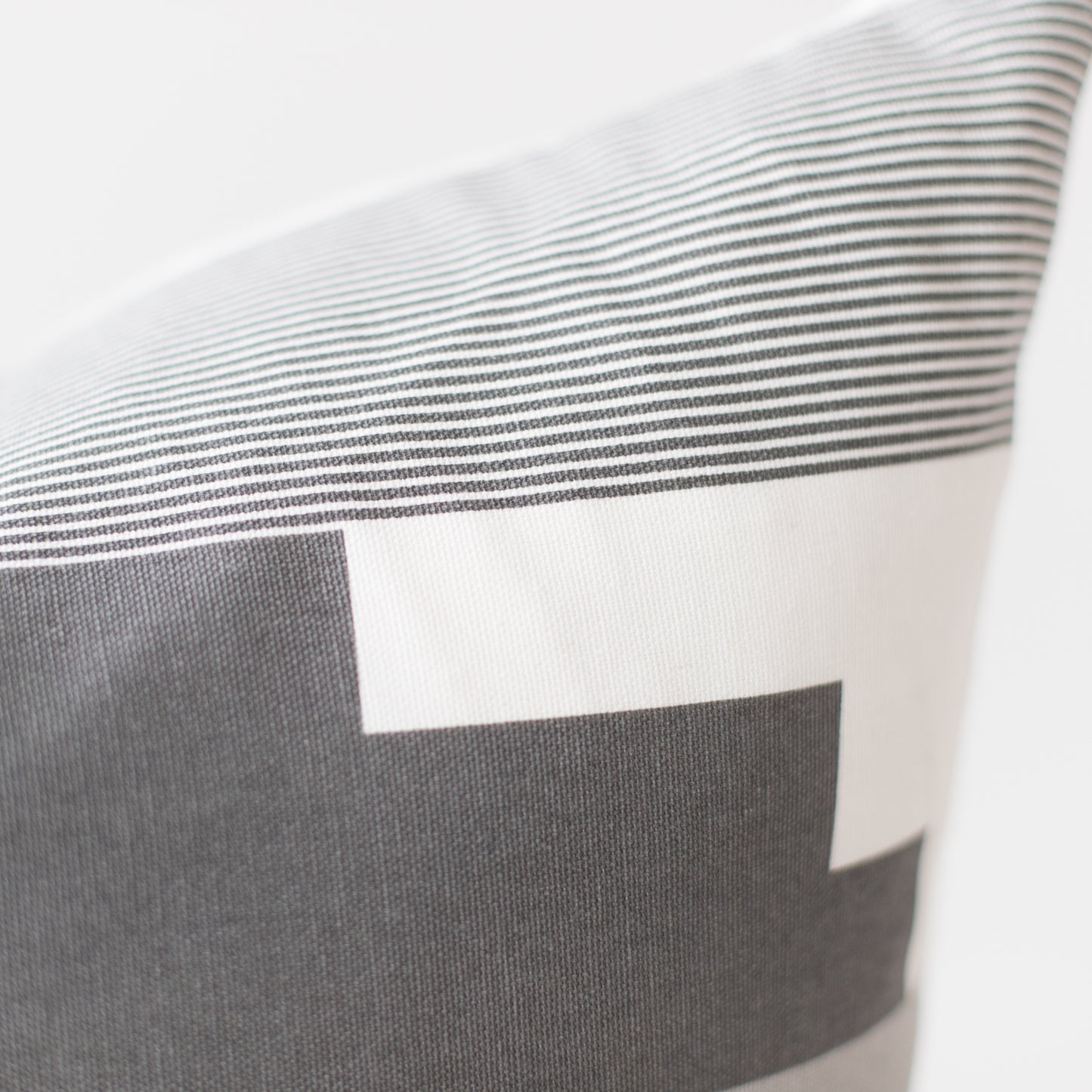 Pillow with gray and white striped pattern and color block design in neutral tones.