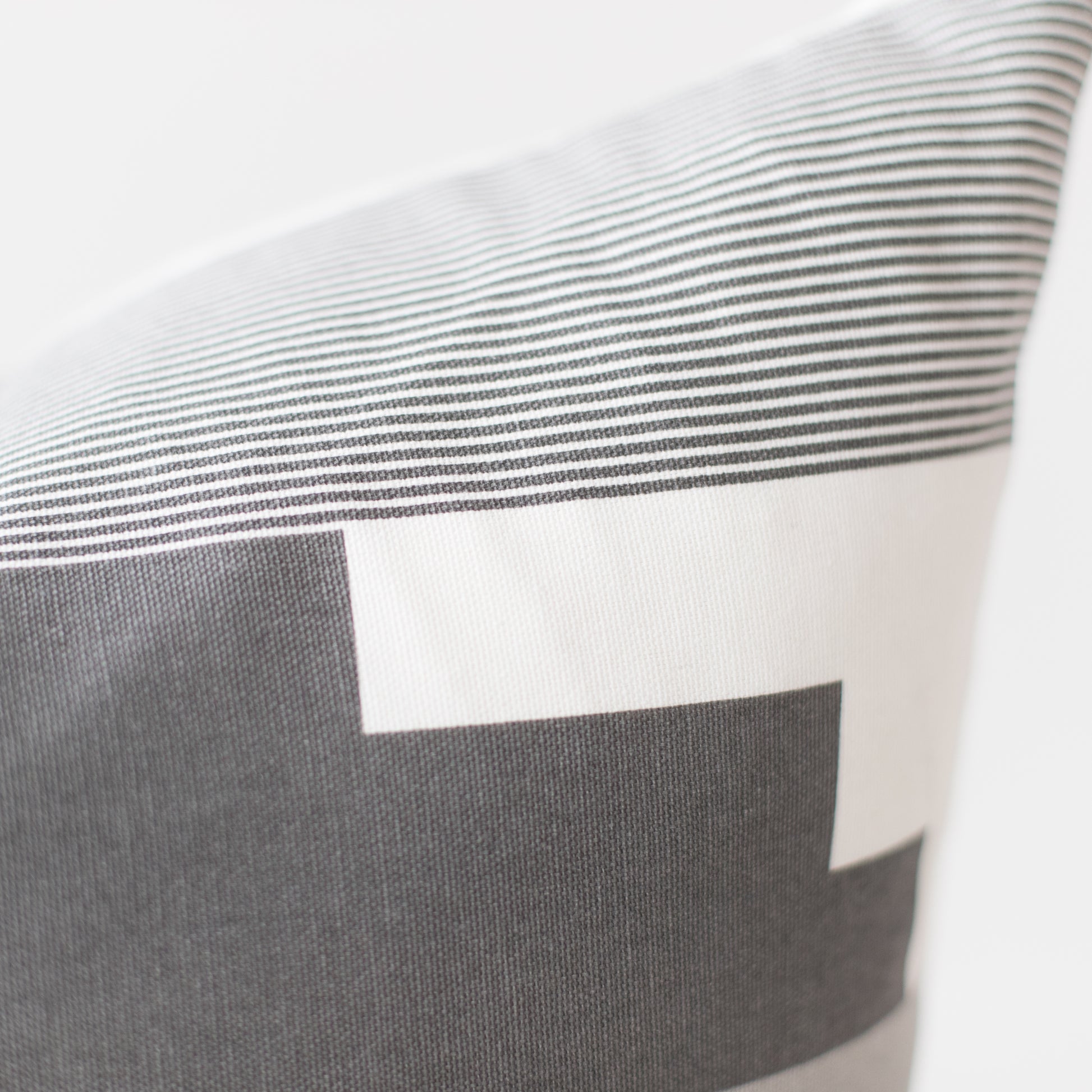 Pillow with gray and white striped pattern and color block design in neutral tones.