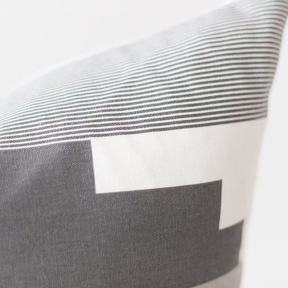 Pillow with gray and white striped pattern and color block design in neutral tones.