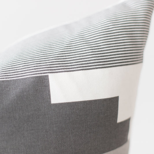 Pillow with gray and white striped pattern and color block design in neutral tones.