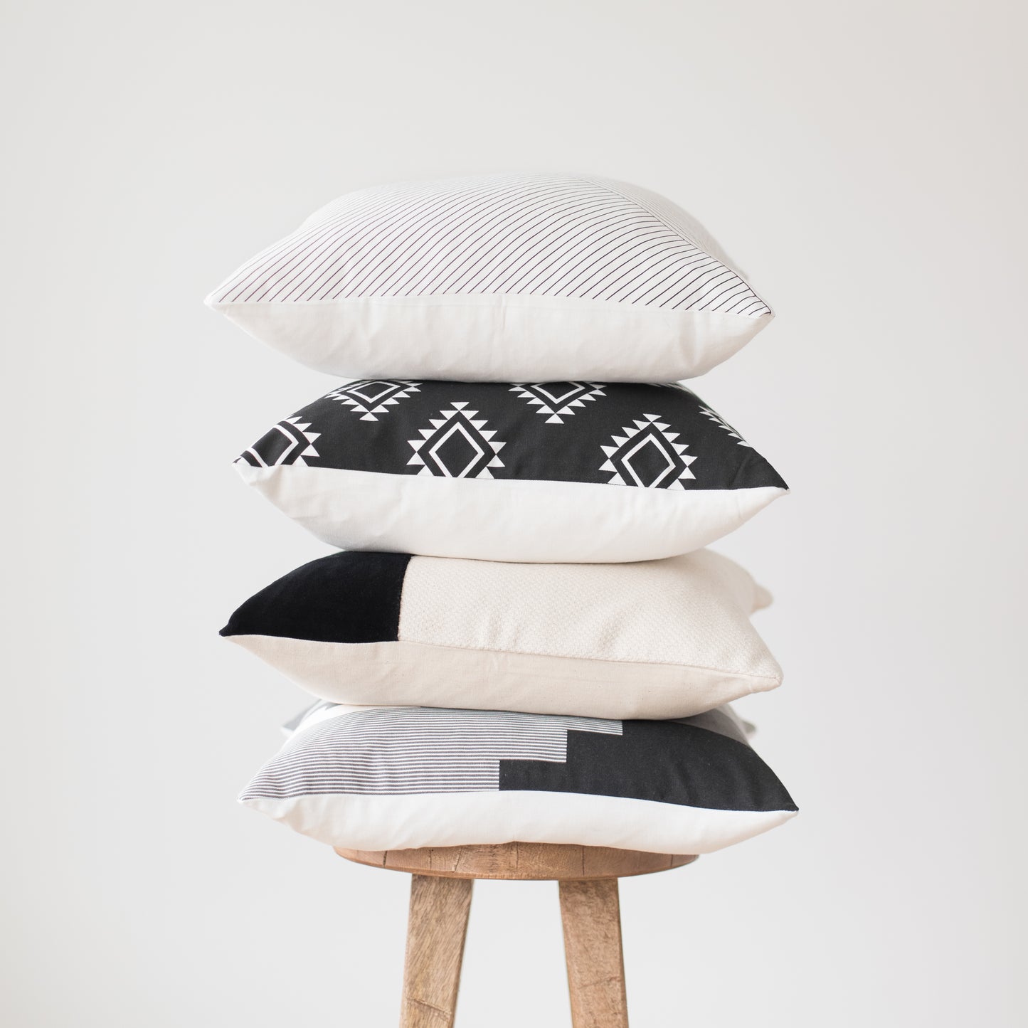 Four 18-inch decorative pillows stacked vertically, featuring striped, geometric, solid, and color-block patterns in black, w