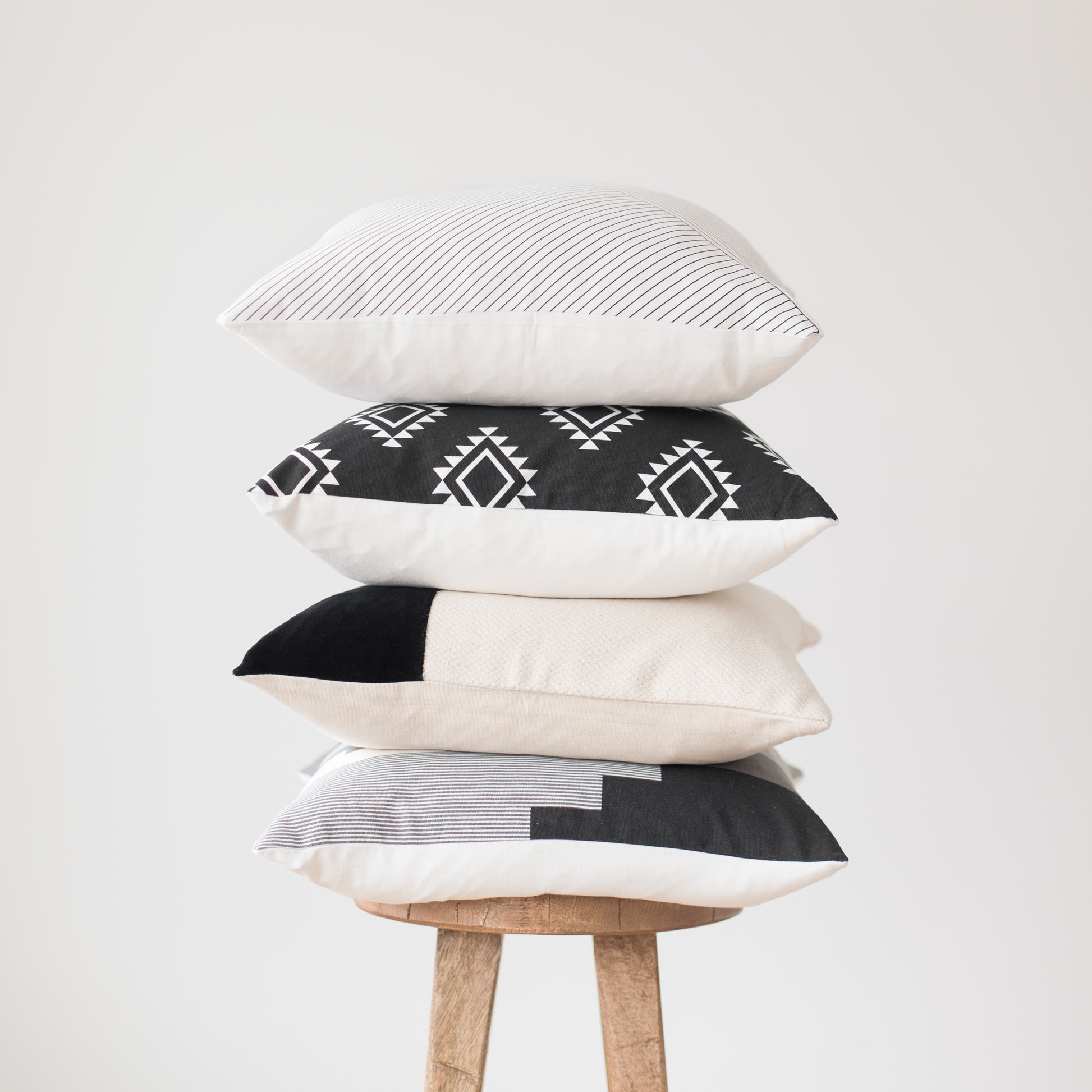 Four 18-inch decorative pillows stacked vertically, featuring striped, geometric, solid, and color-block patterns in black, w