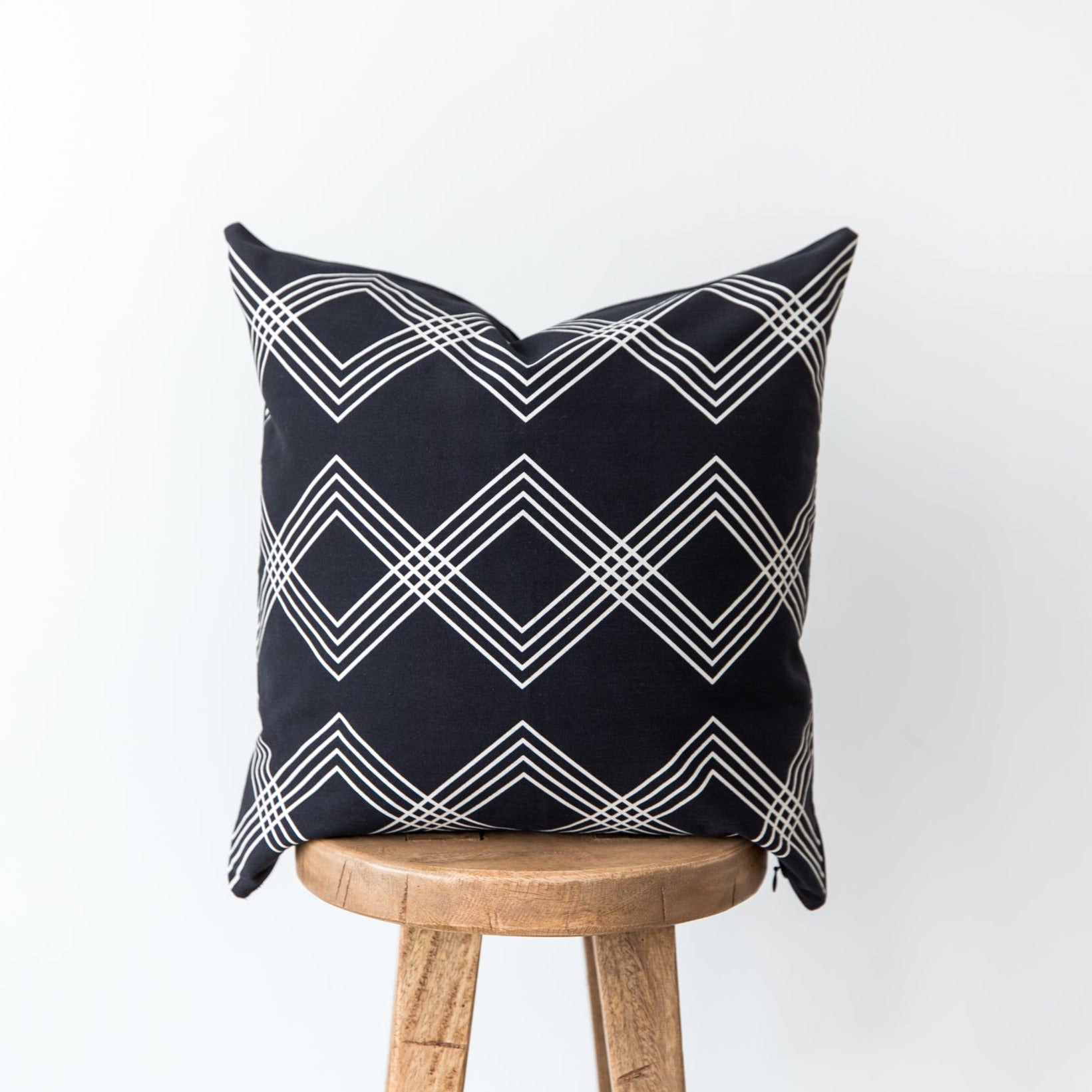 Black and white geometric patterned throw pillow with diamond and chevron design draped over wooden stool.