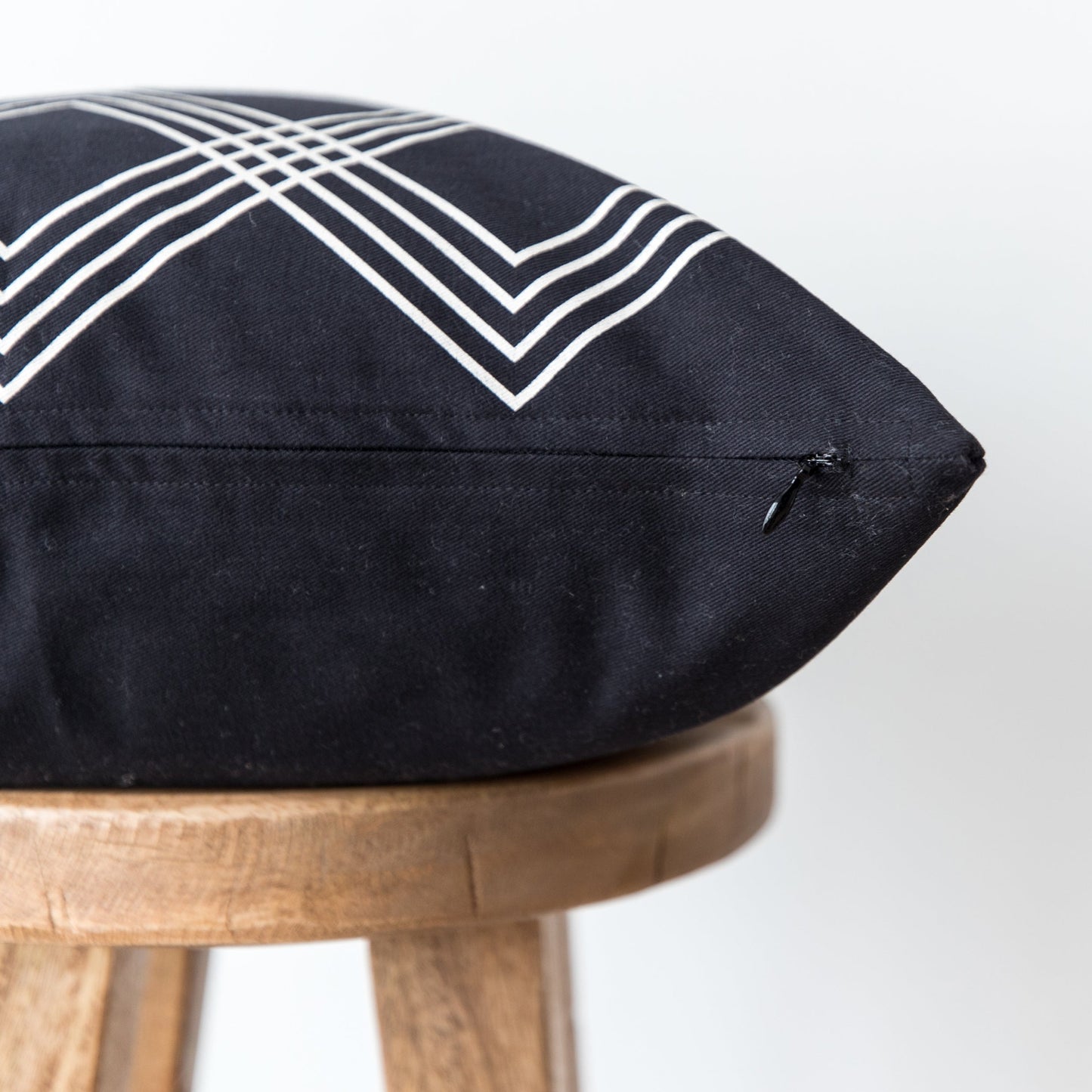 Black cushion pillow with white geometric chevron pattern on wooden stool.