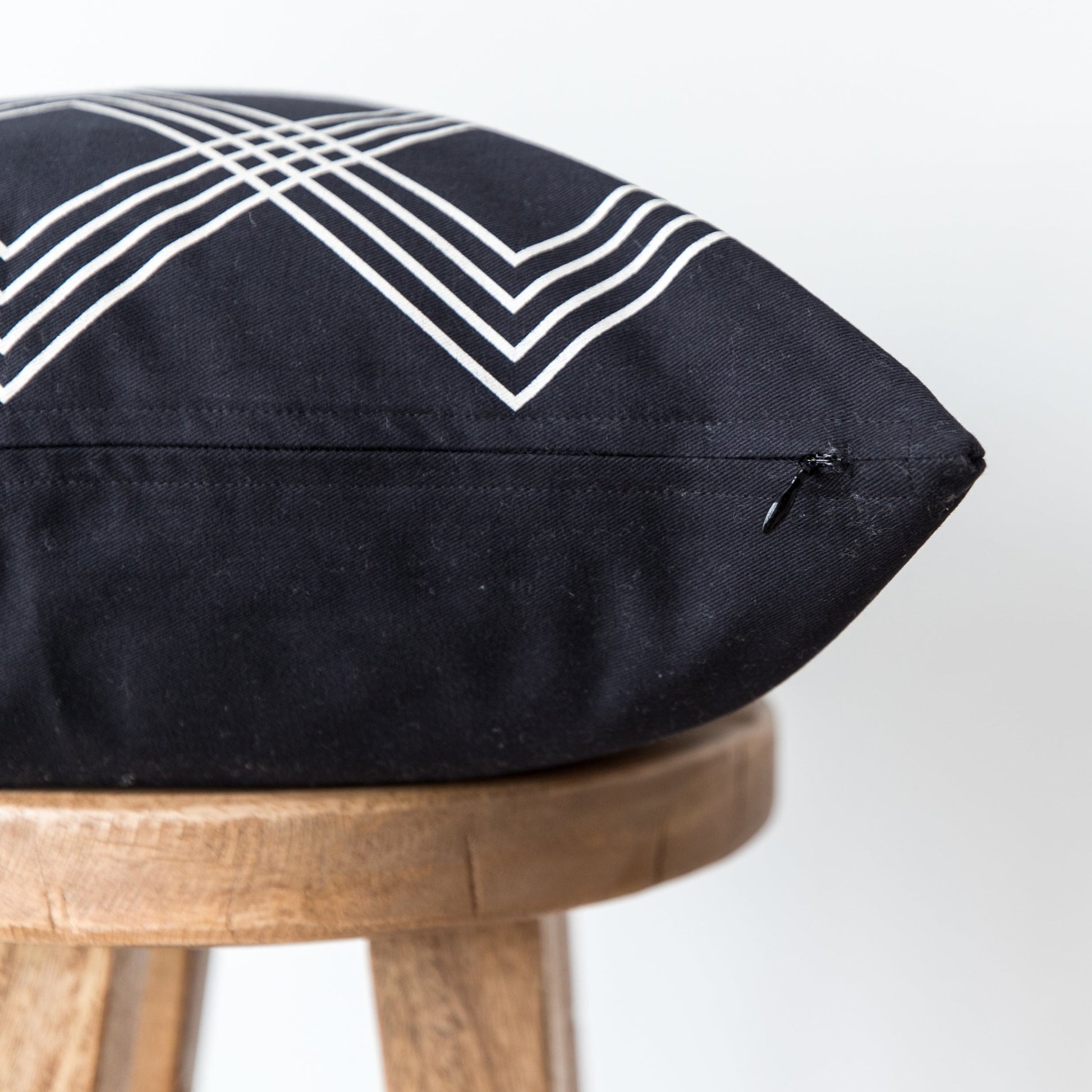 Black cushion pillow with white geometric chevron pattern on wooden stool.