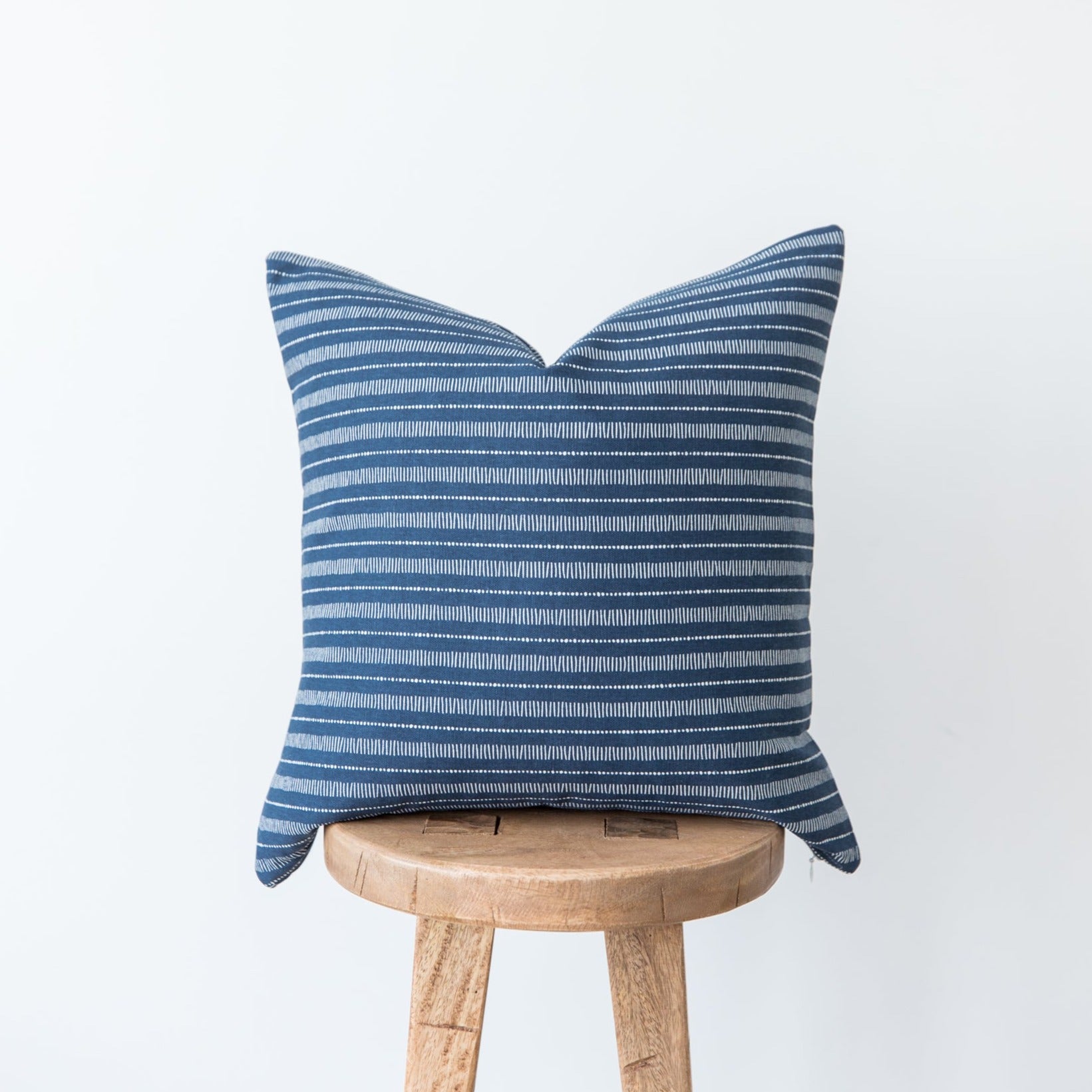 Blue and white striped pillow cover with horizontal lines displayed on wooden stool.