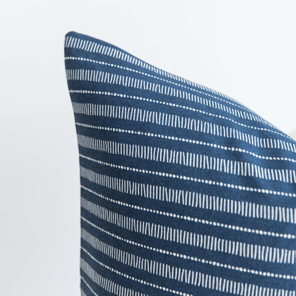Blue pillow with white striped and dotted geometric pattern, shown at an angle against white background.