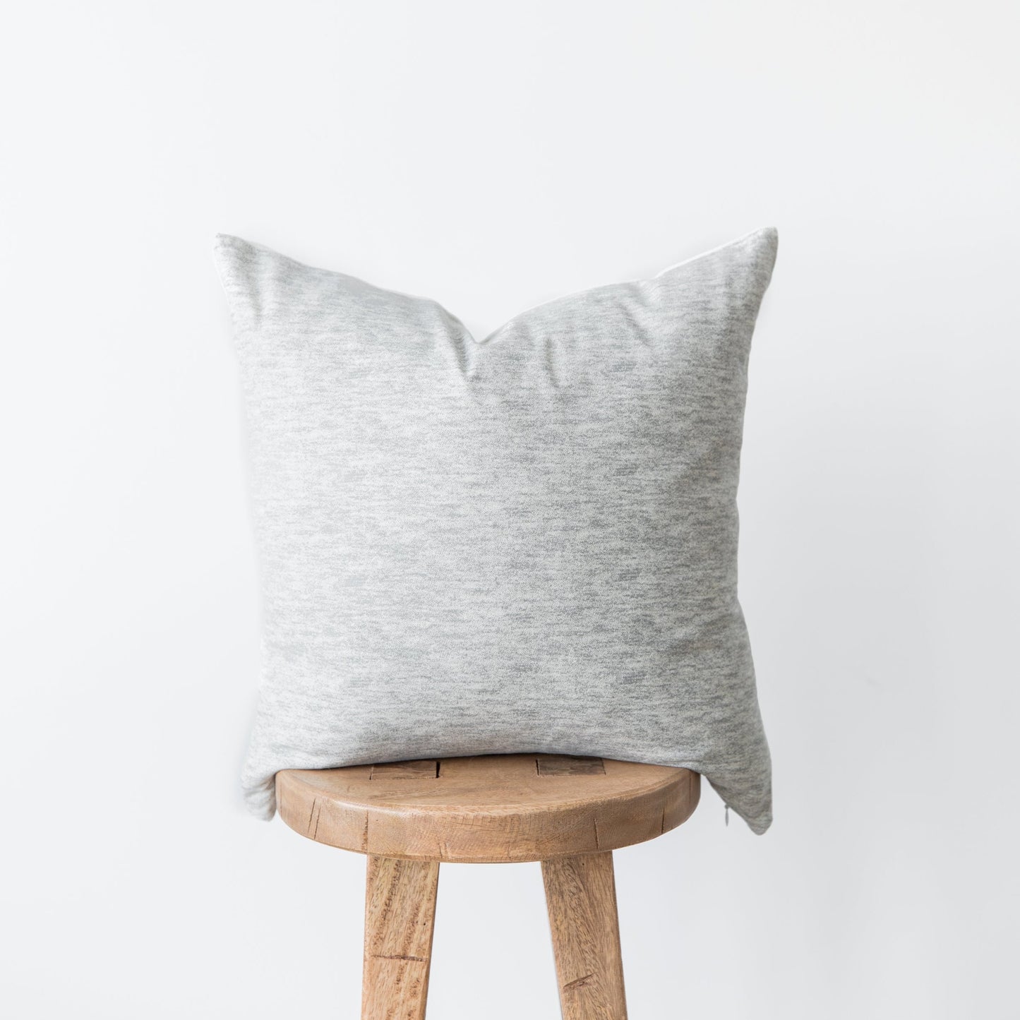 Light gray linen pillow cover draped over a wooden stool.
