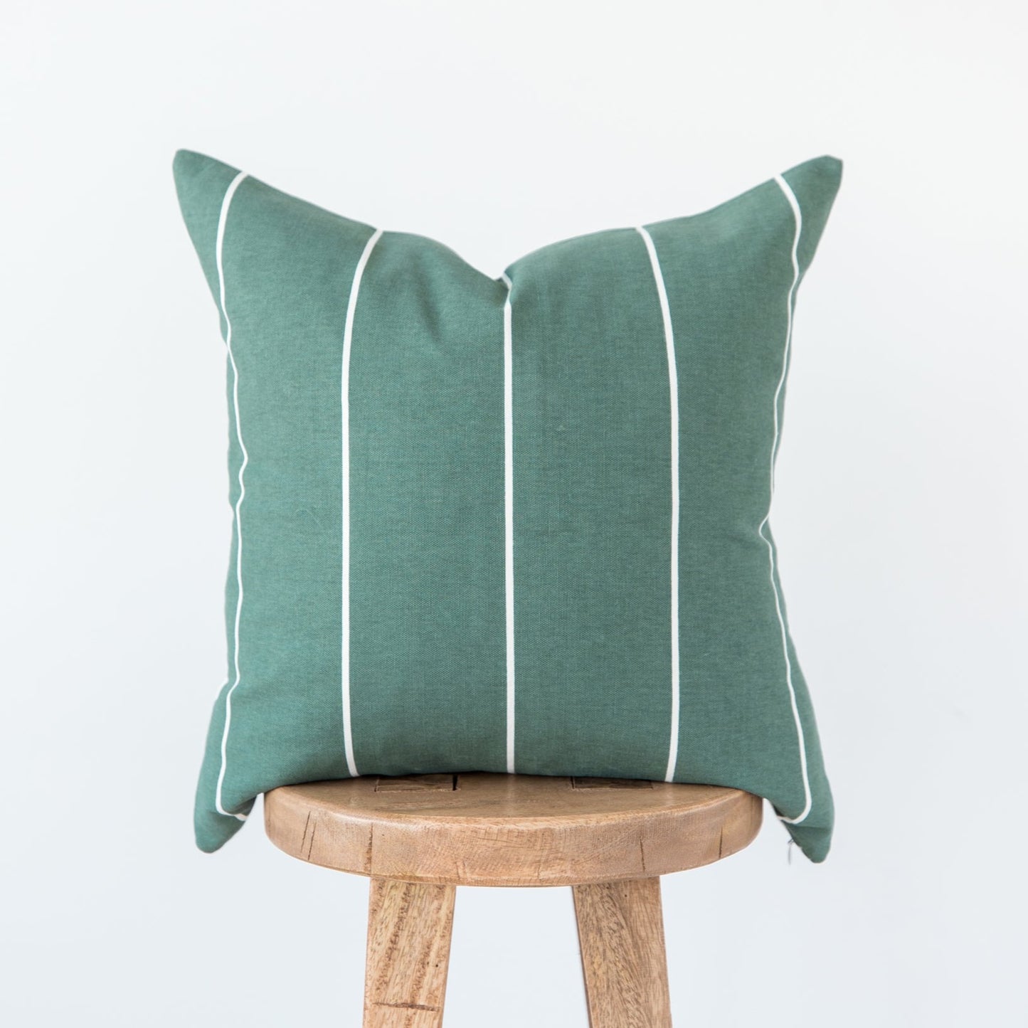 Green linen pillow with white vertical stripes and piping, displayed on wooden stool.