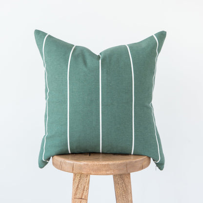 Green linen pillow with white vertical stripes and piping, displayed on wooden stool.