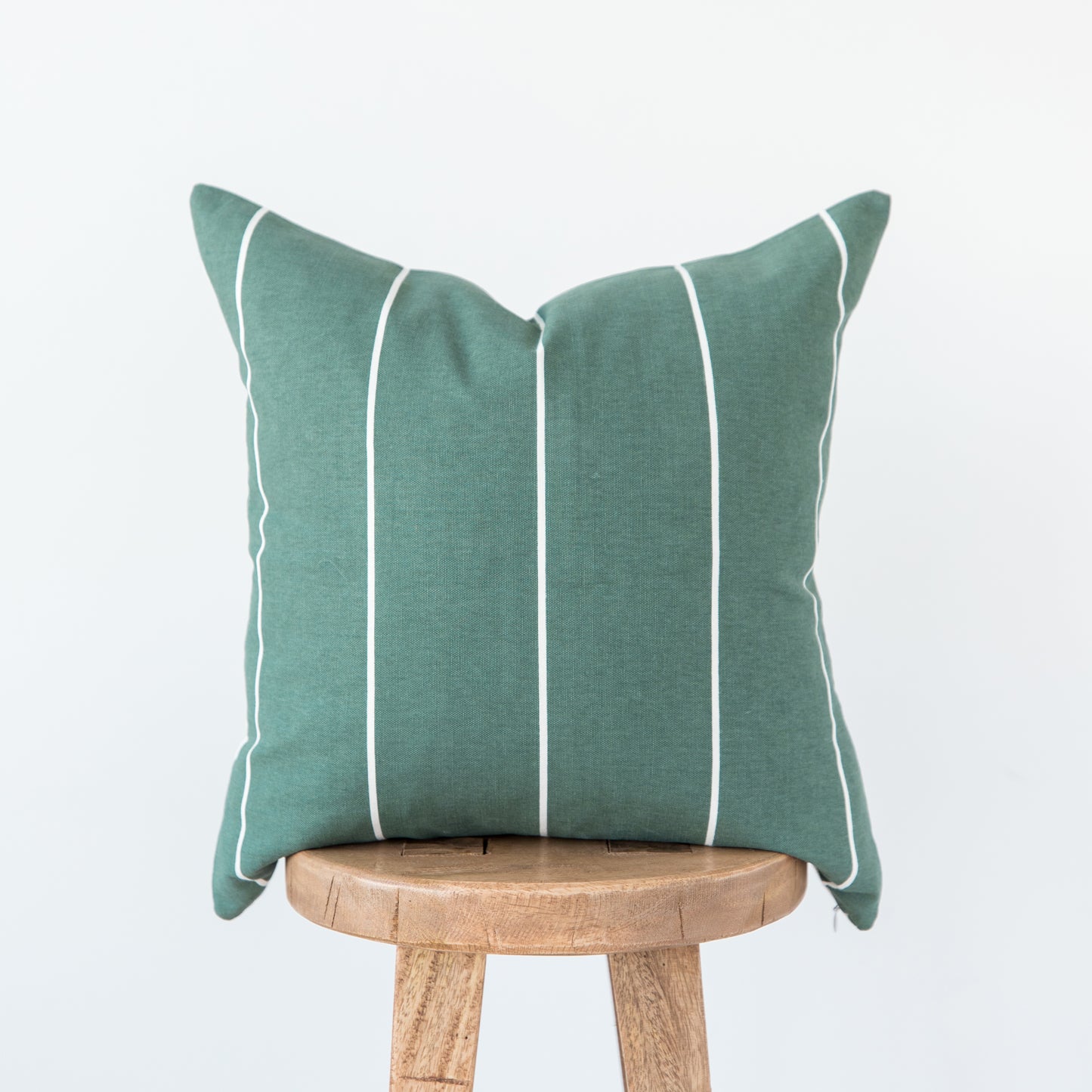 Teal linen pillow with white vertical stripe detailing, displayed on a wooden stool.