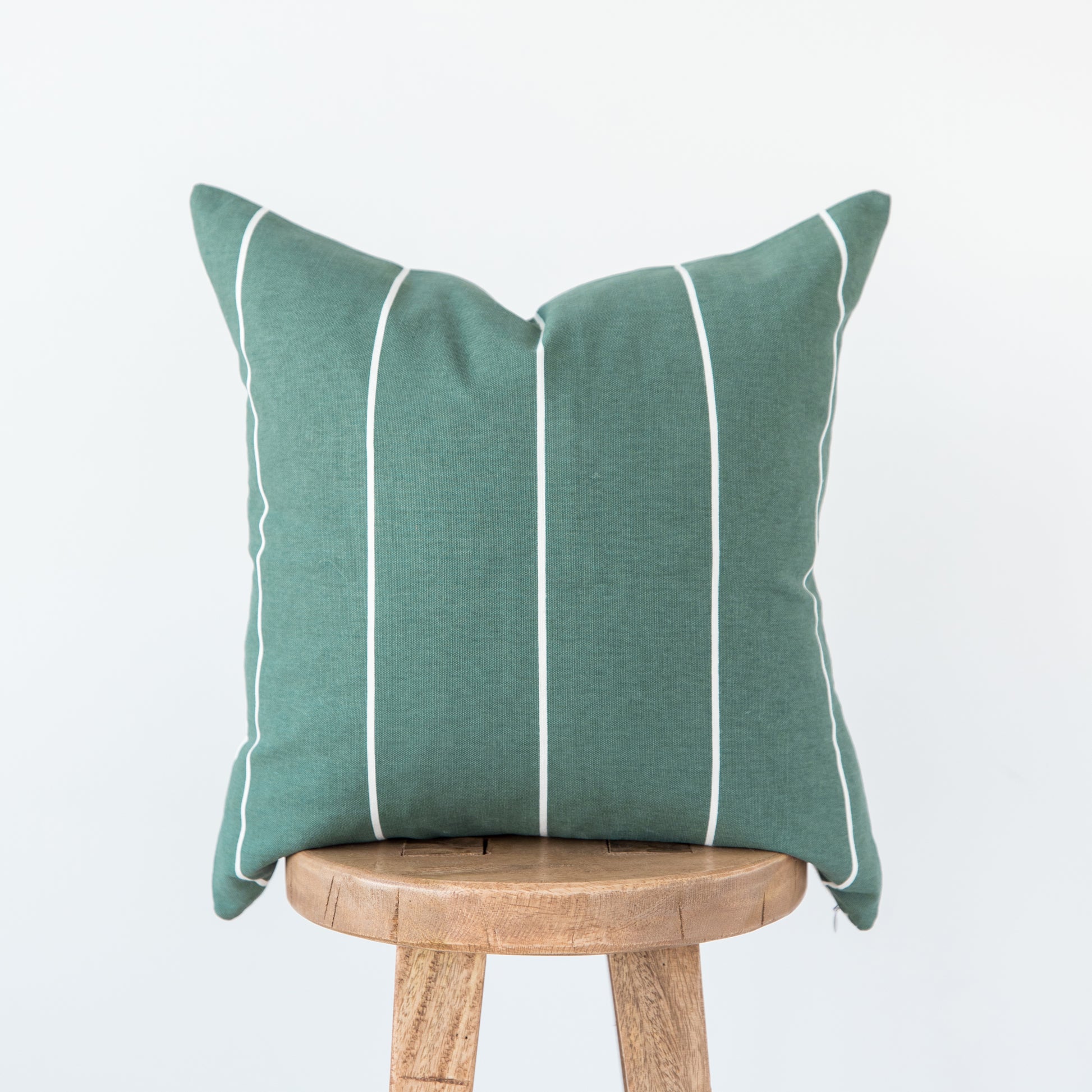 Teal linen pillow with white vertical stripe detailing, displayed on a wooden stool.