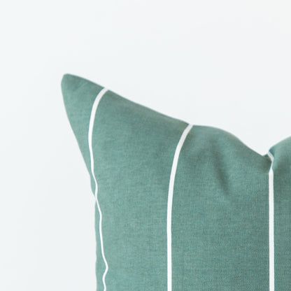 Sage green decorative pillow with white piping trim along the edges.