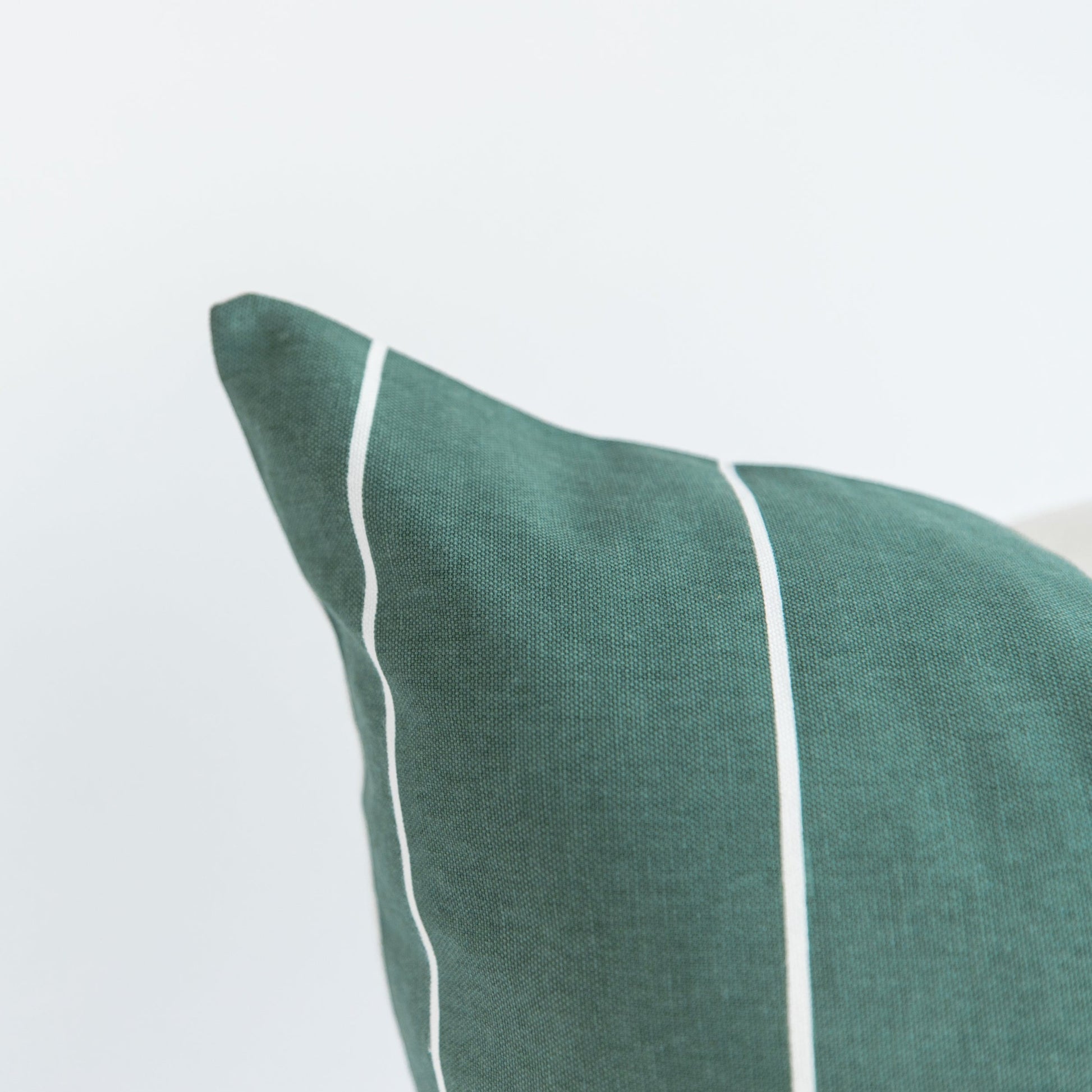 Sage green woven pillow with white piping along vertical seams, 18 inches.