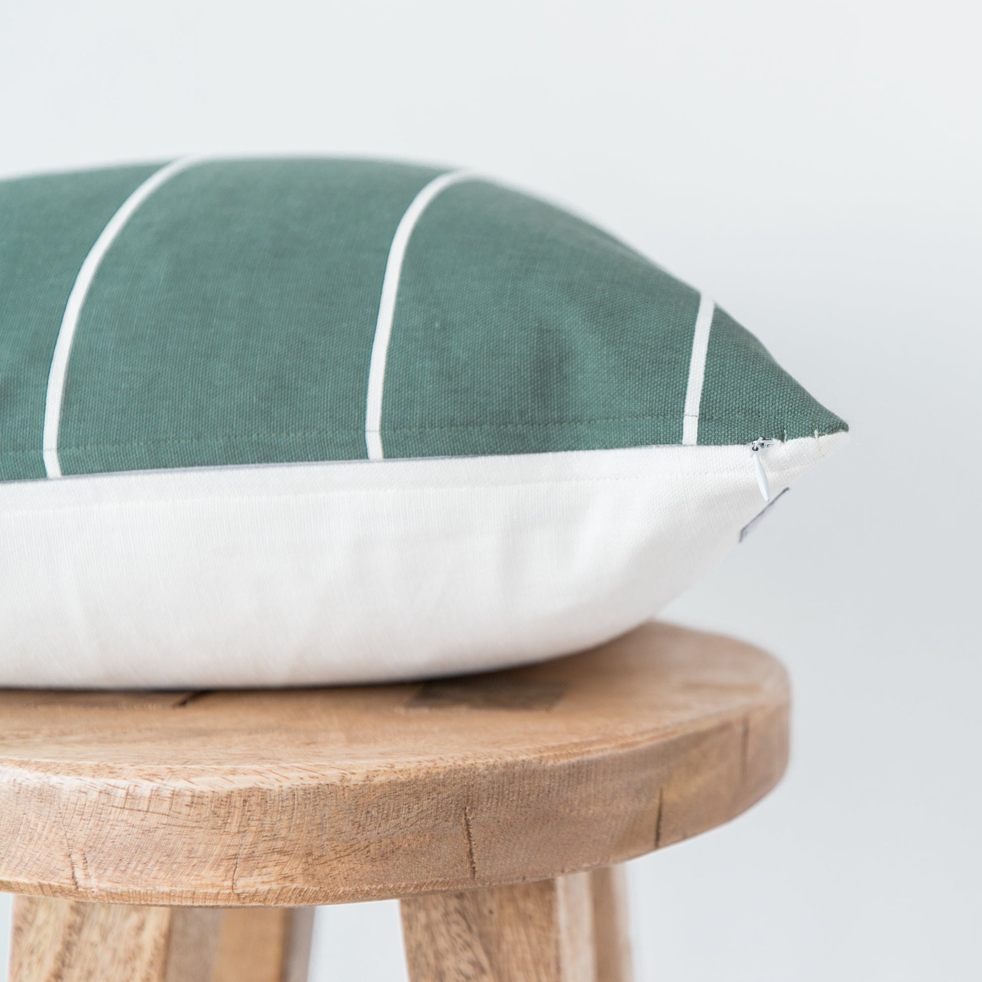 Sage green pillow with white stripes and cream linen base, displayed on wooden stool.