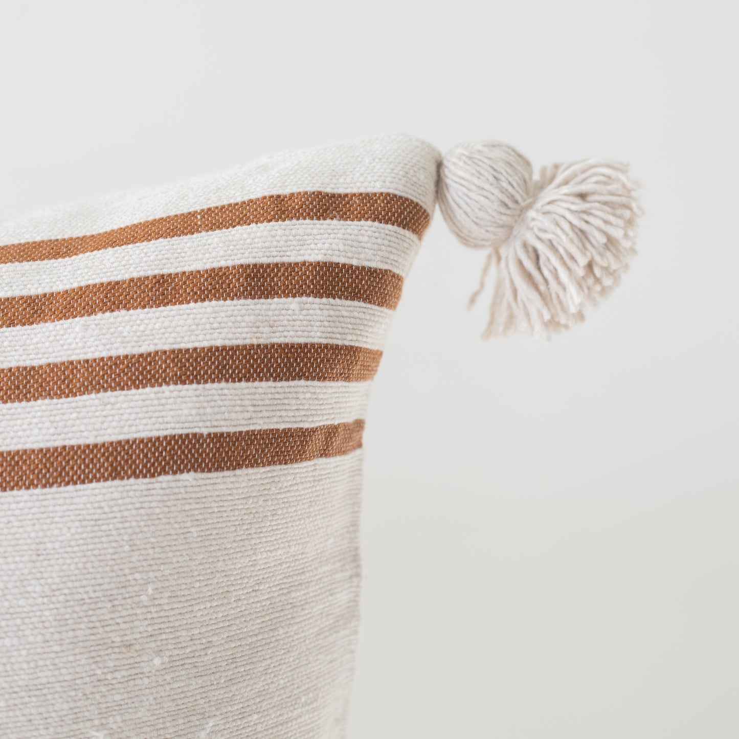 Cream cushion with tan horizontal stripes and cream corner tassels, 22 inches.