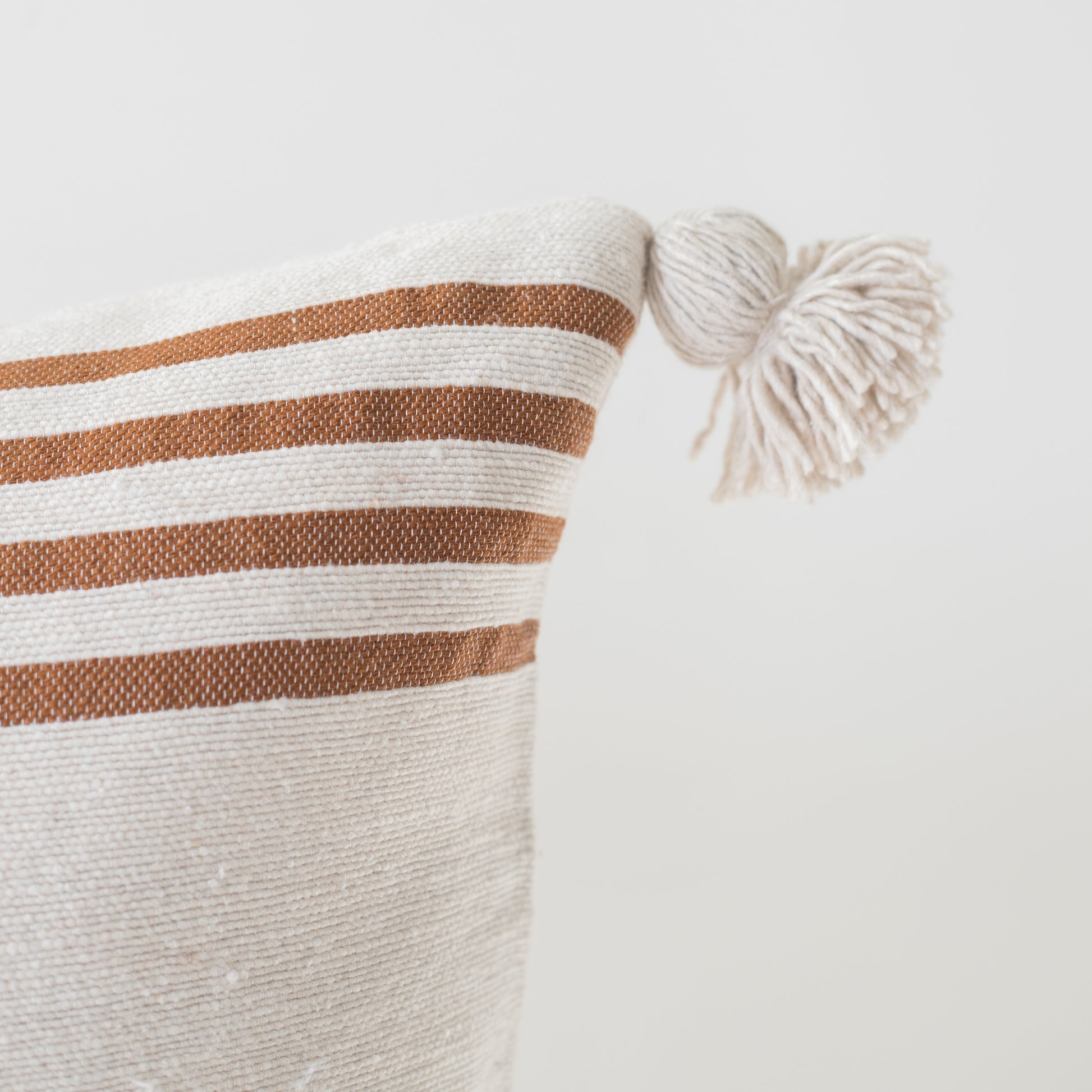 Cream cushion with tan horizontal stripes and cream corner tassels, 22 inches.